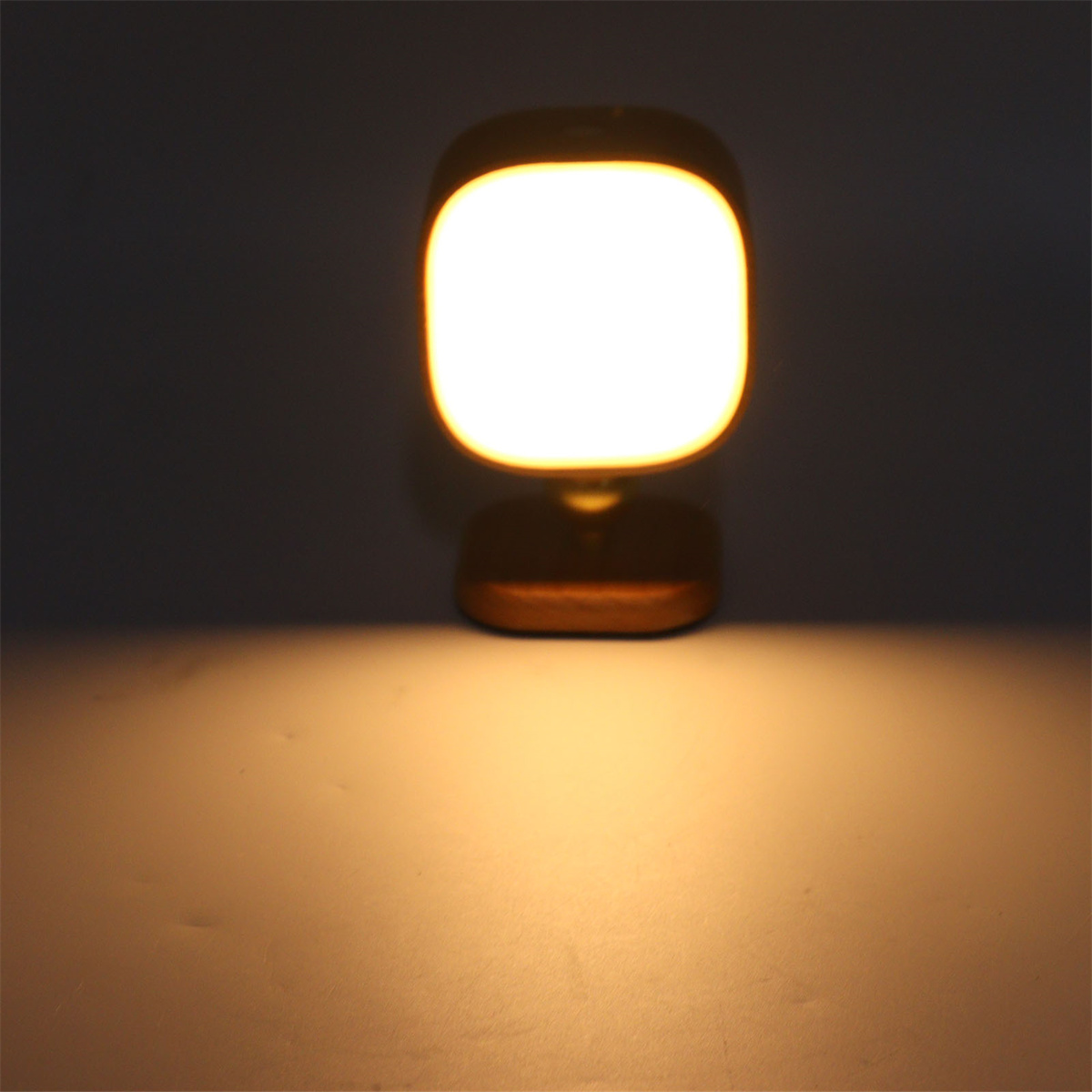 Eine quadratische Lampe mit warmem, gelbem Schein steht auf einer Oberfläche und leuchtet.