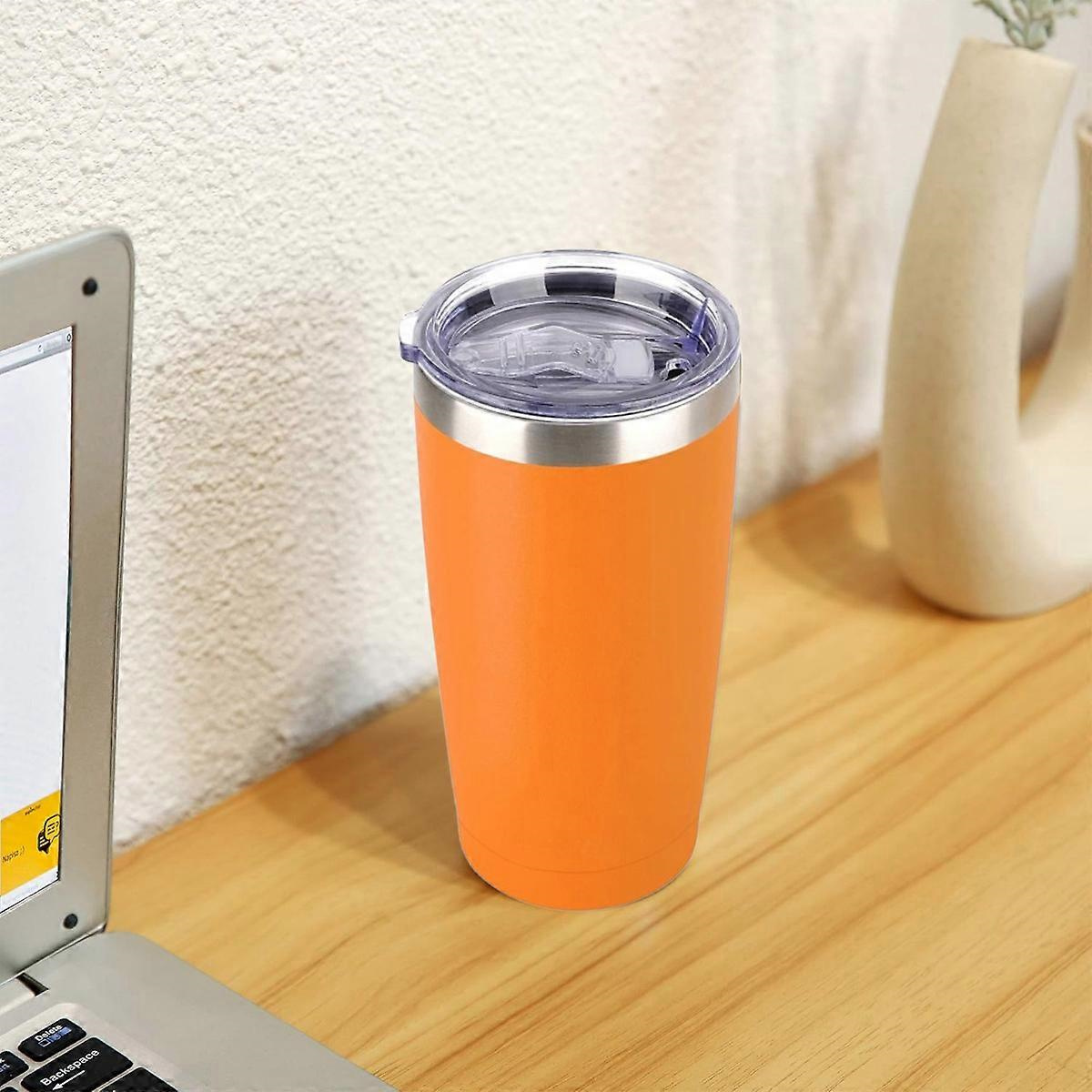 Ein orangefarbener Reisebecher mit durchsichtigem Deckel steht auf einer Holzoberfläche. Ein Laptop und eine Vase sind in der Nähe.