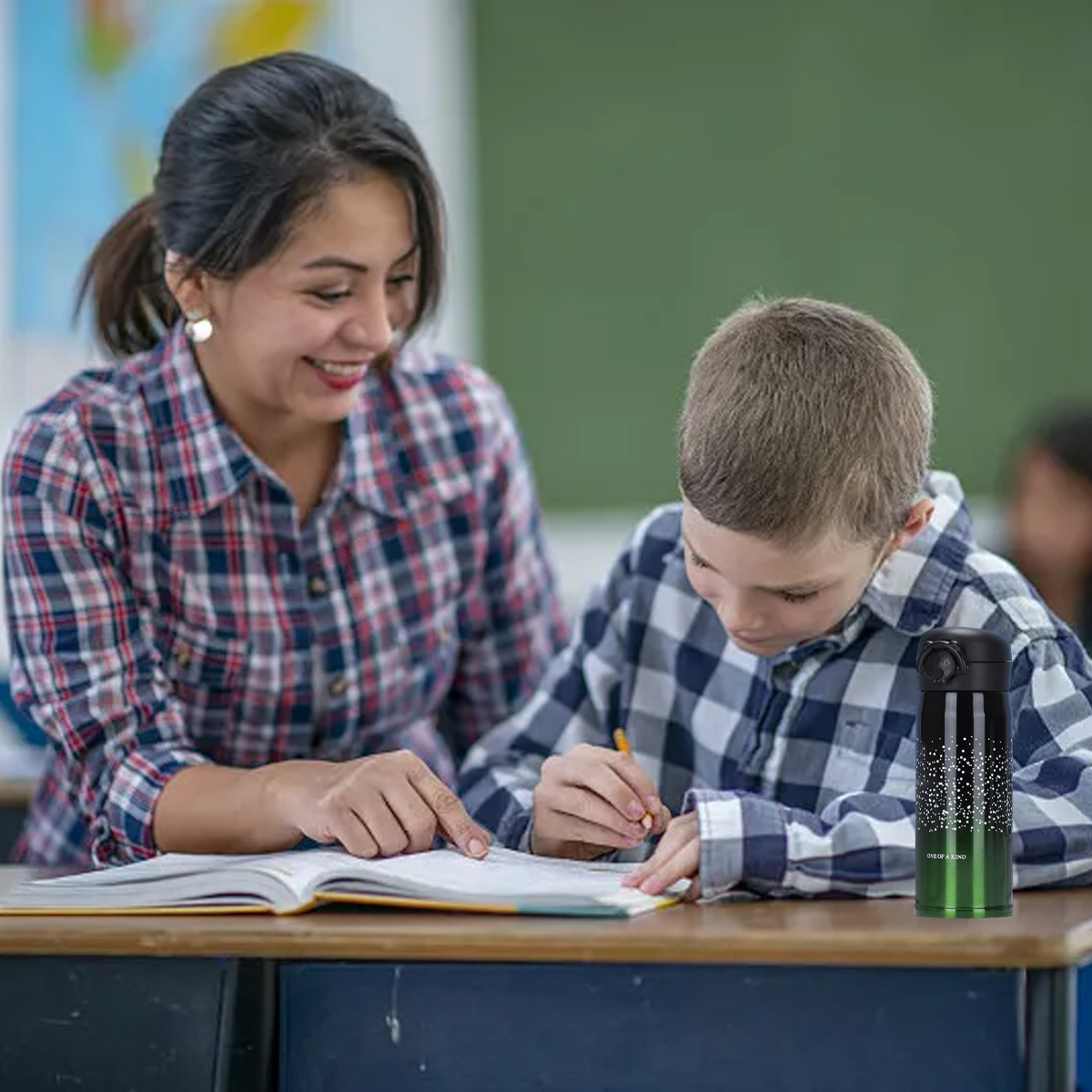 Eine Lehrerin hilft einem Schüler an einem Schreibtisch. Auf dem Schreibtisch steht eine Wasserflasche. Beide lächeln.