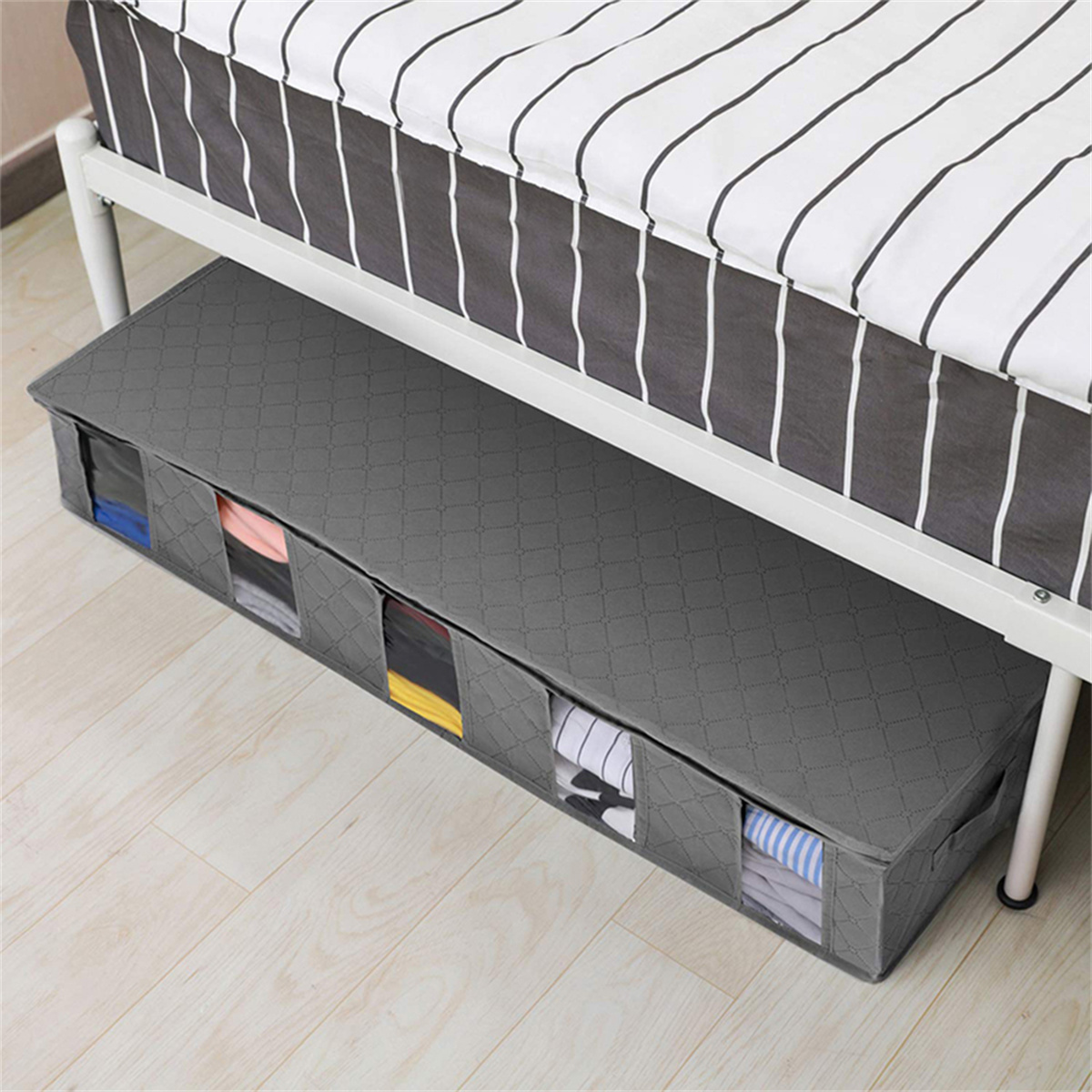 Ein grauer Aufbewahrungsbehälter unter dem Bett mit mehreren transparenten Fenstern, die Kleidung zeigen. Es ist unter einem Bett.