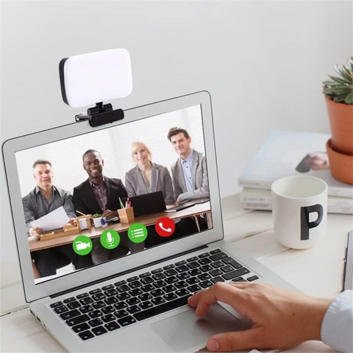 Ein Laptop-Bildschirm zeigt einen Videoanruf mit vier Personen. Oben befindet sich eine Webcam-Leuchte. Eine Hand berührt die Tastatur.