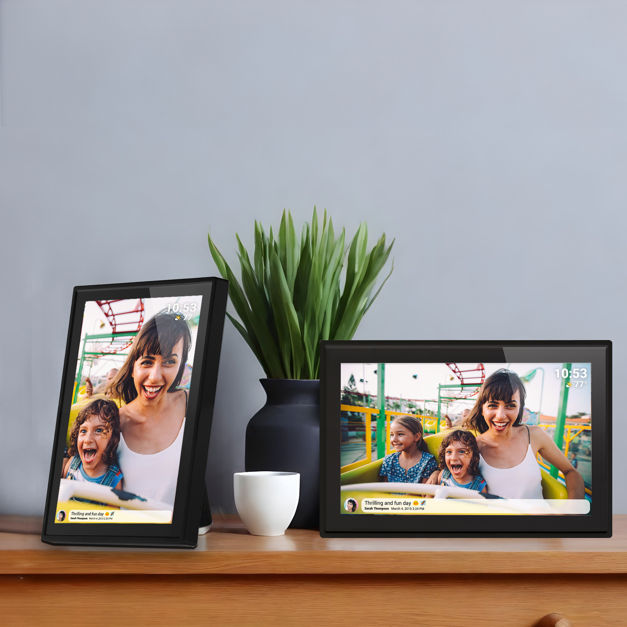 Deux cadres photo numériques noirs affichant des photos. Comprend une plante et une tasse blanche. Surface en bois.