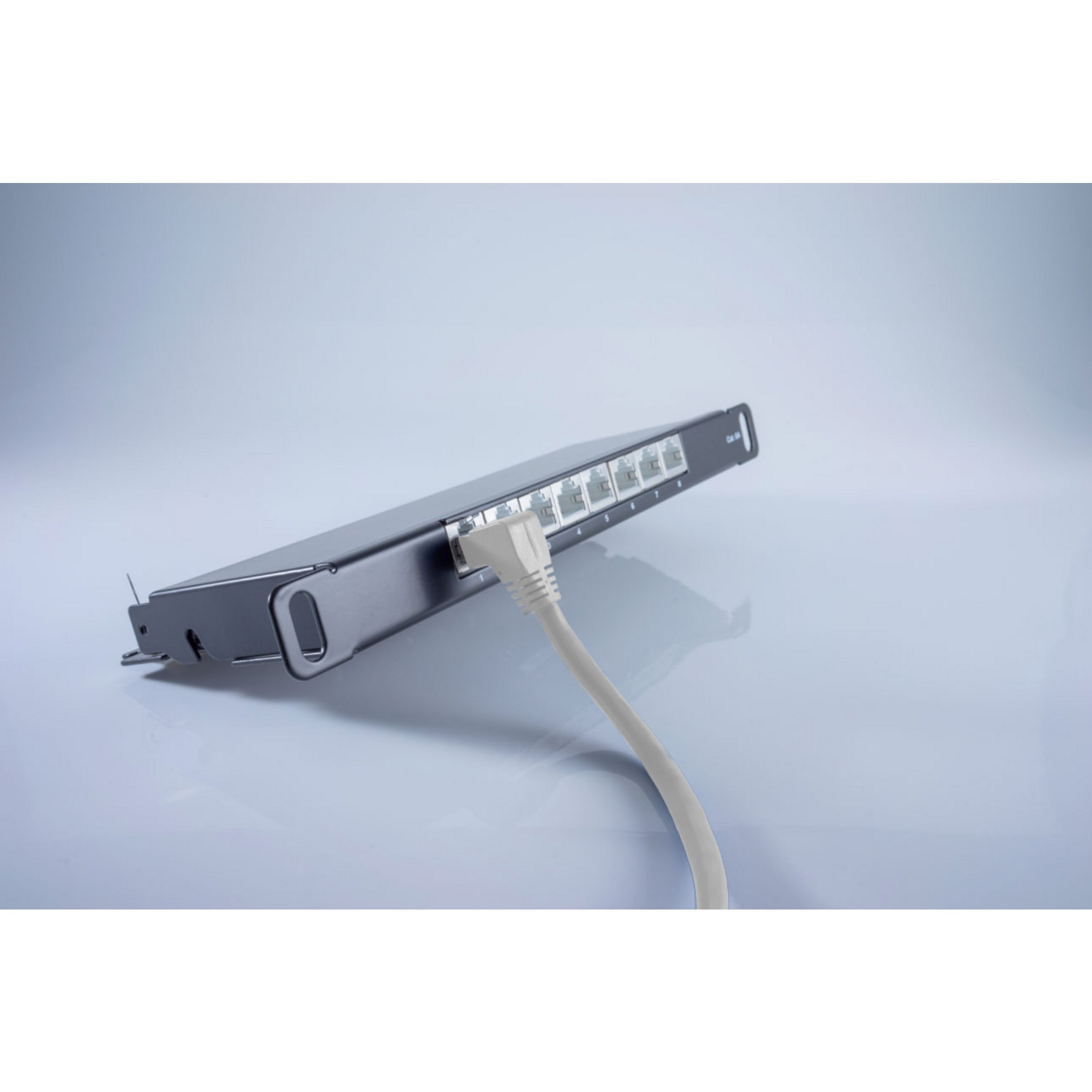 Switch di rete con cavo ethernet collegato, su una superficie sfumata bianca e grigia.