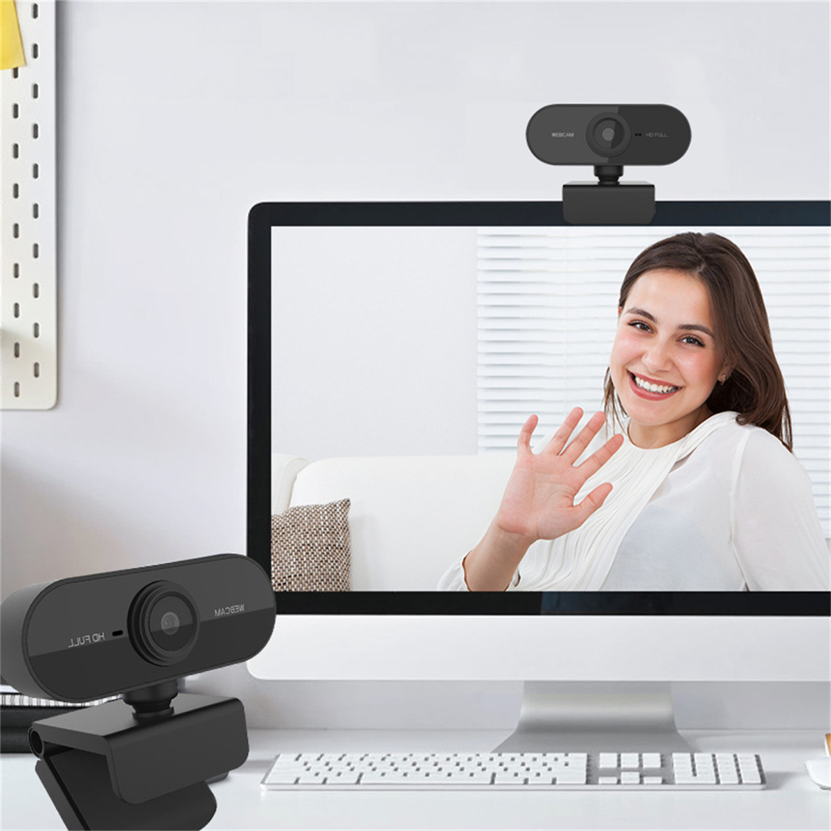 Eine Frau winkt von einem Computerbildschirm; zwei Webcams auf einem Schreibtisch, eine auf dem Monitor und eine darunter.