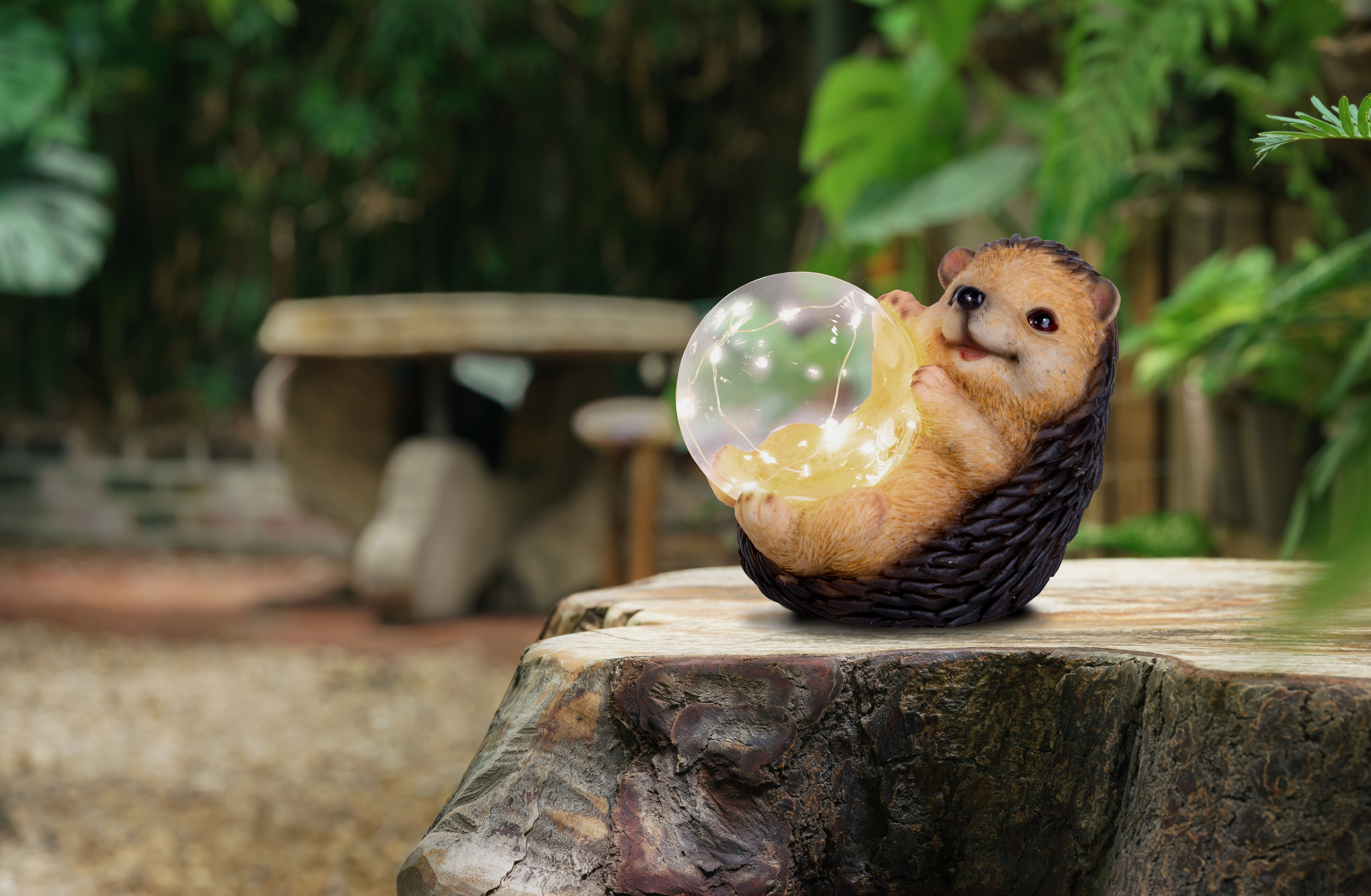 Igeldeko mit Lichtern, sitzt auf Baumstumpf, verschwommener Gartenhintergrund.