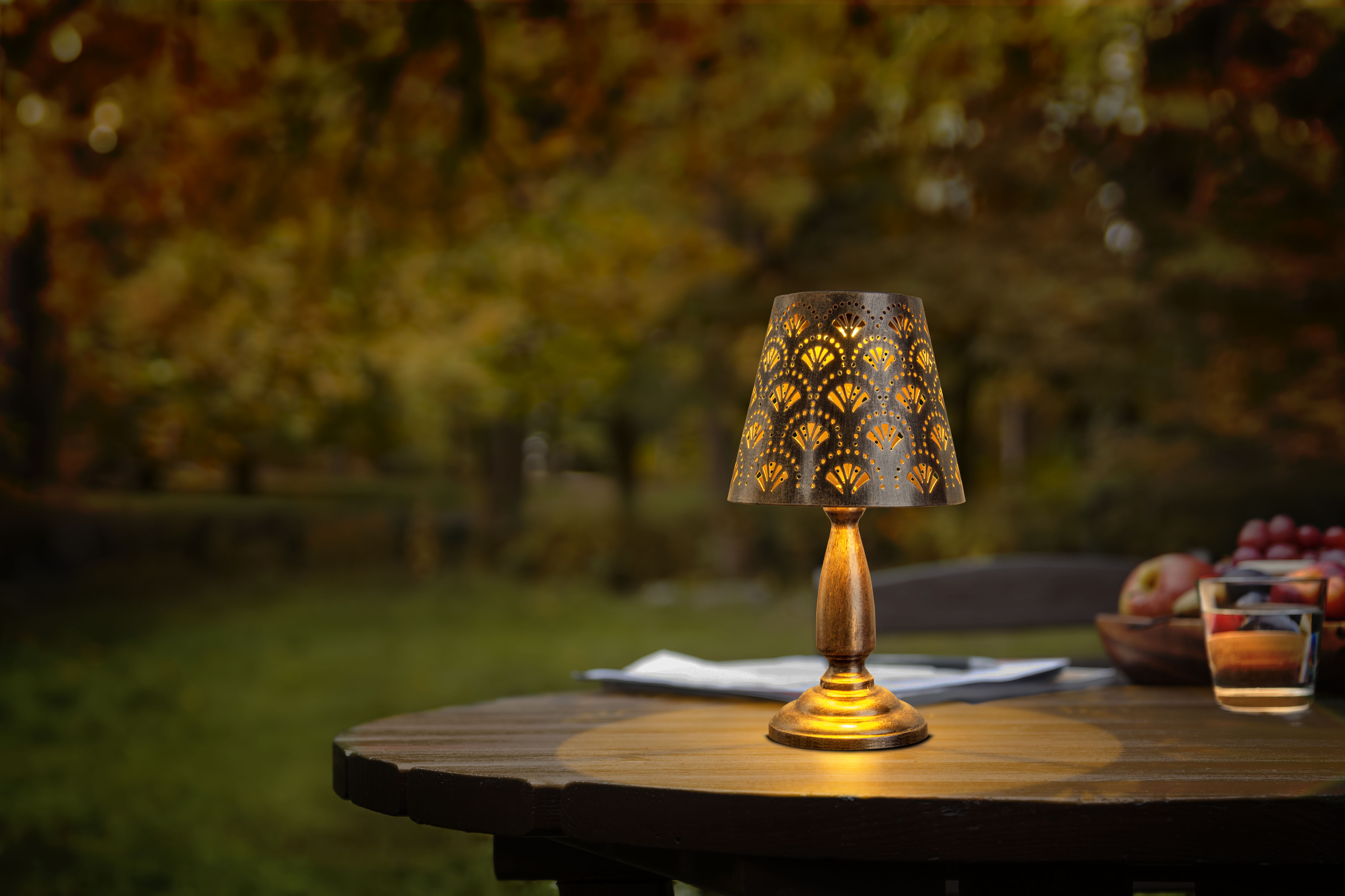 Eine beleuchtete Lampe auf einem Holztisch mit verschwommenem Hintergrund mit Bäumen und Grün.
