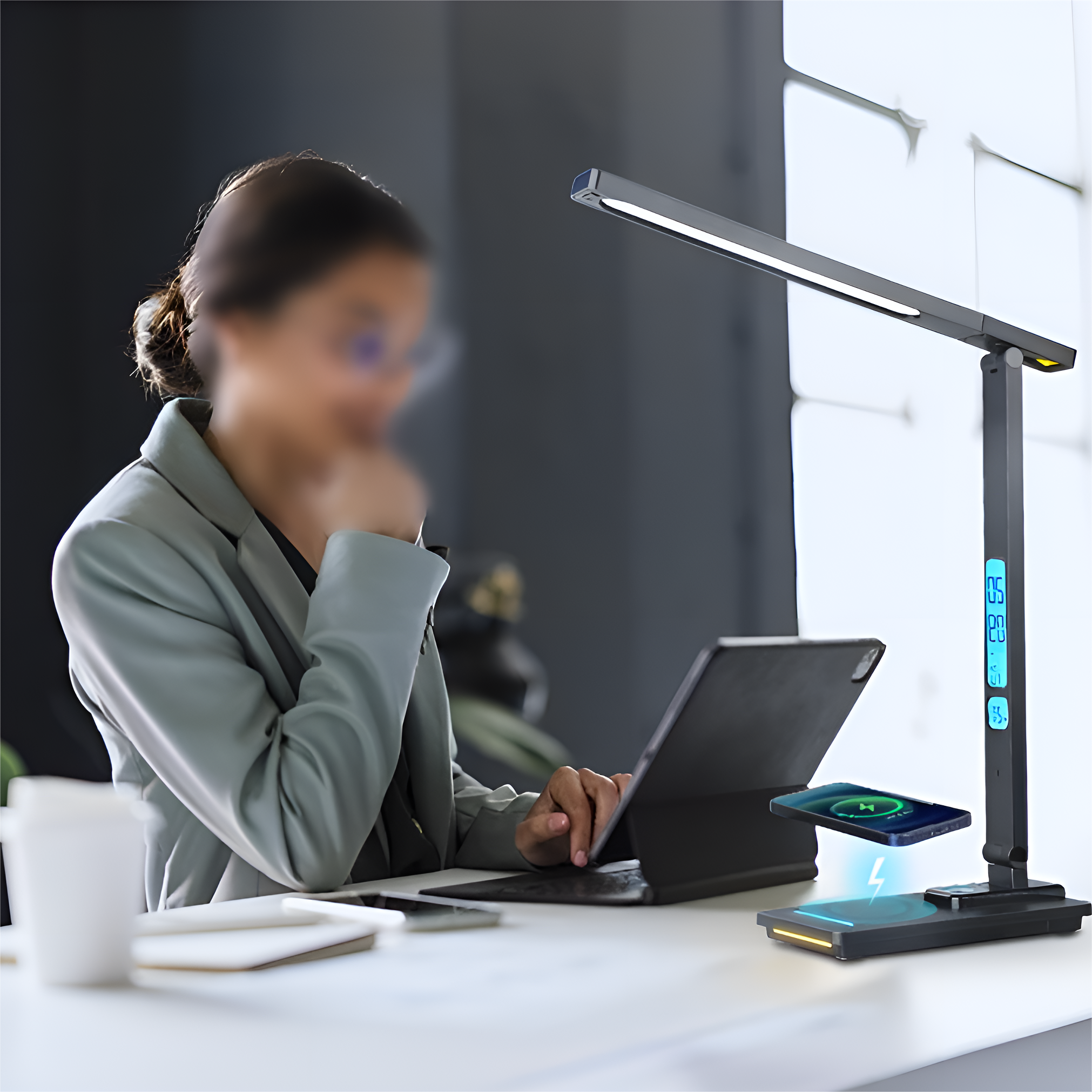 Frau am Schreibtisch, die ein Tablet benutzt, neben einer Schreibtischlampe mit kabellosem Laden.