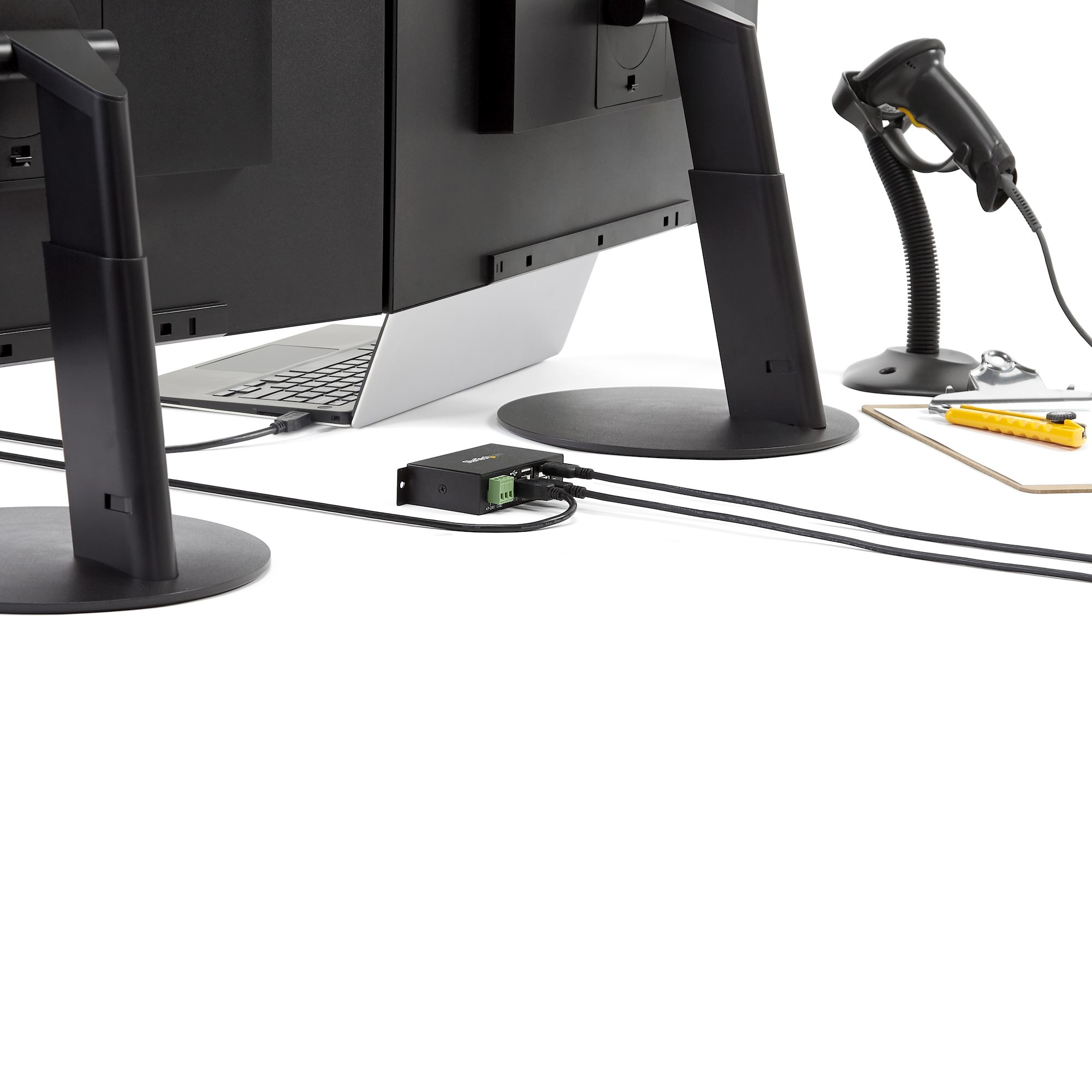 Configurazione ufficio con monitor, laptop, scanner e cavi, su sfondo bianco.