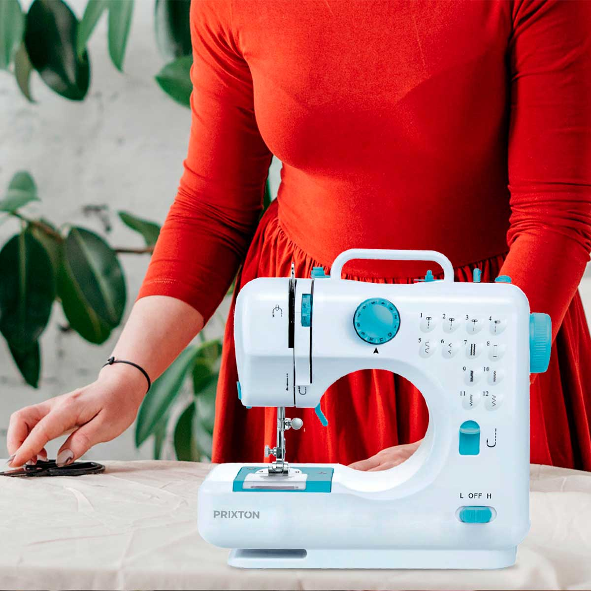 Kobieta szyje na białej i turkusowej maszynie do szycia, czerwona sukienka, drewniany stół.