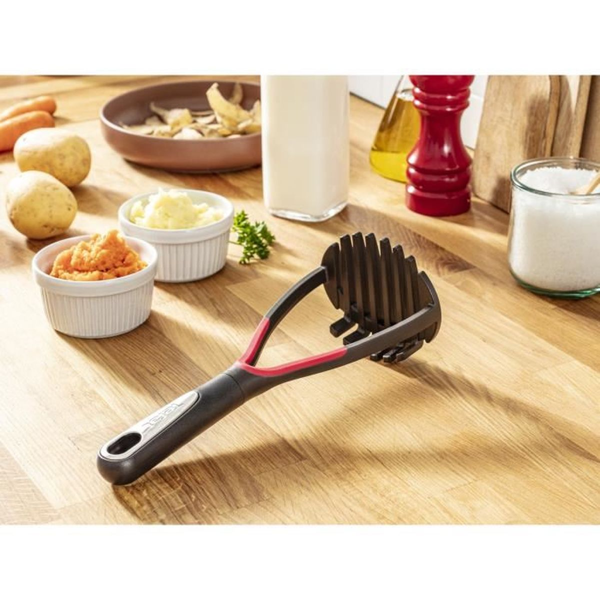 Kartoffelstampfer auf Holztisch mit Zutaten und Utensilien.