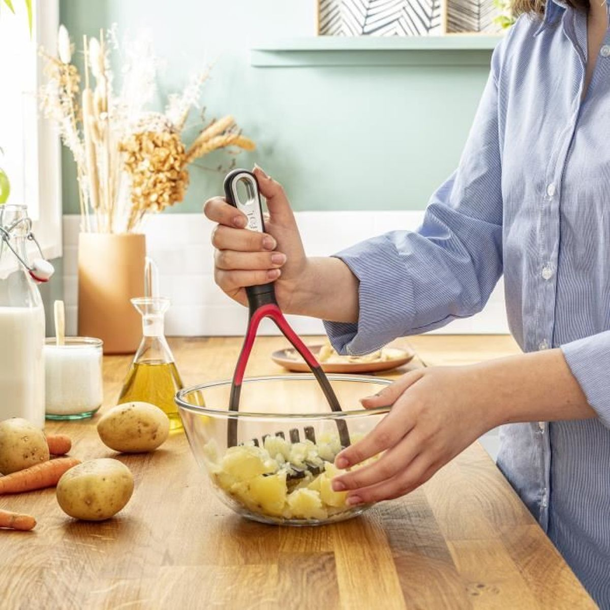 Eine Person zerdrückt Kartoffeln in einer Glasschüssel auf einem Holztisch.