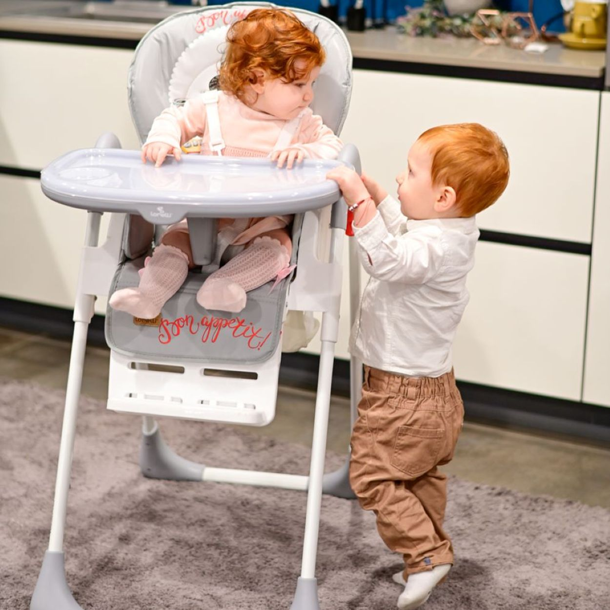 Zwei rothaarige Kleinkinder, eines in einem Hochstuhl, das andere greift danach.