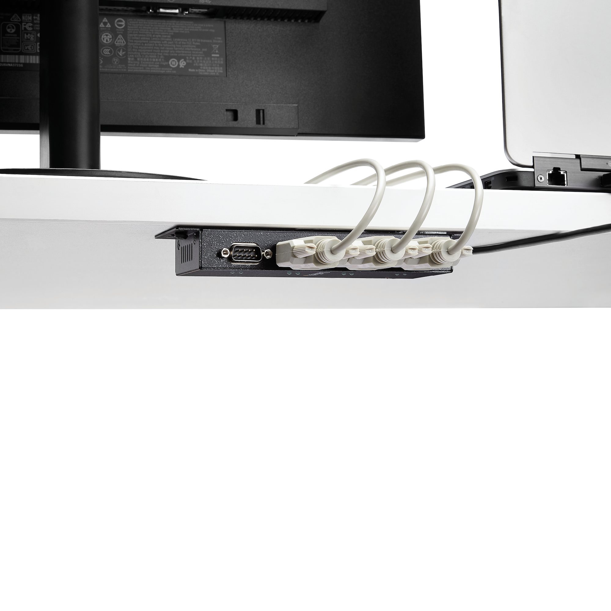 Caja de gestión de cables negra debajo de un escritorio. Varios cables blancos enchufados.