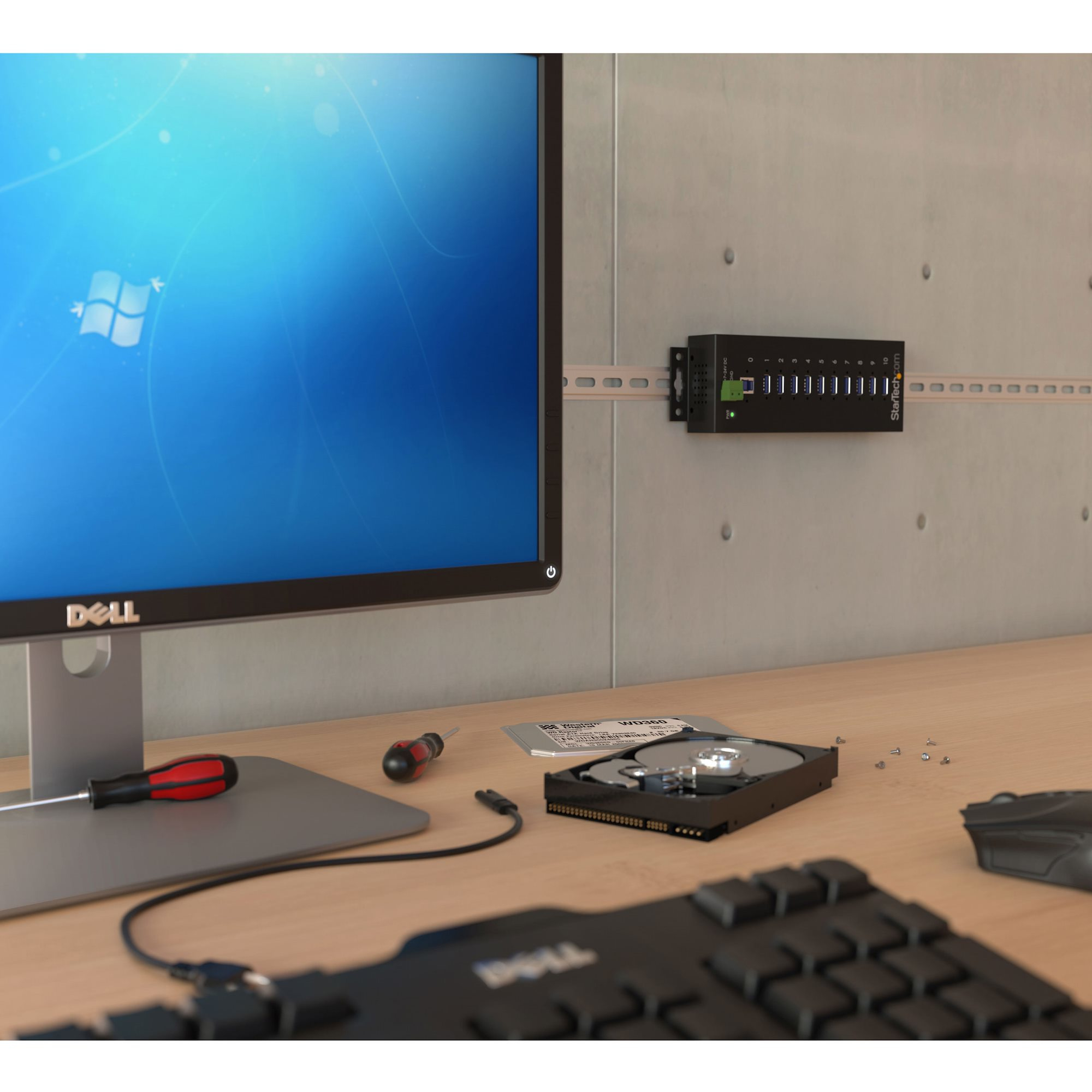 Una configuración de computadora con monitor Dell, teclado, disco duro, destornillador y toma de pared.