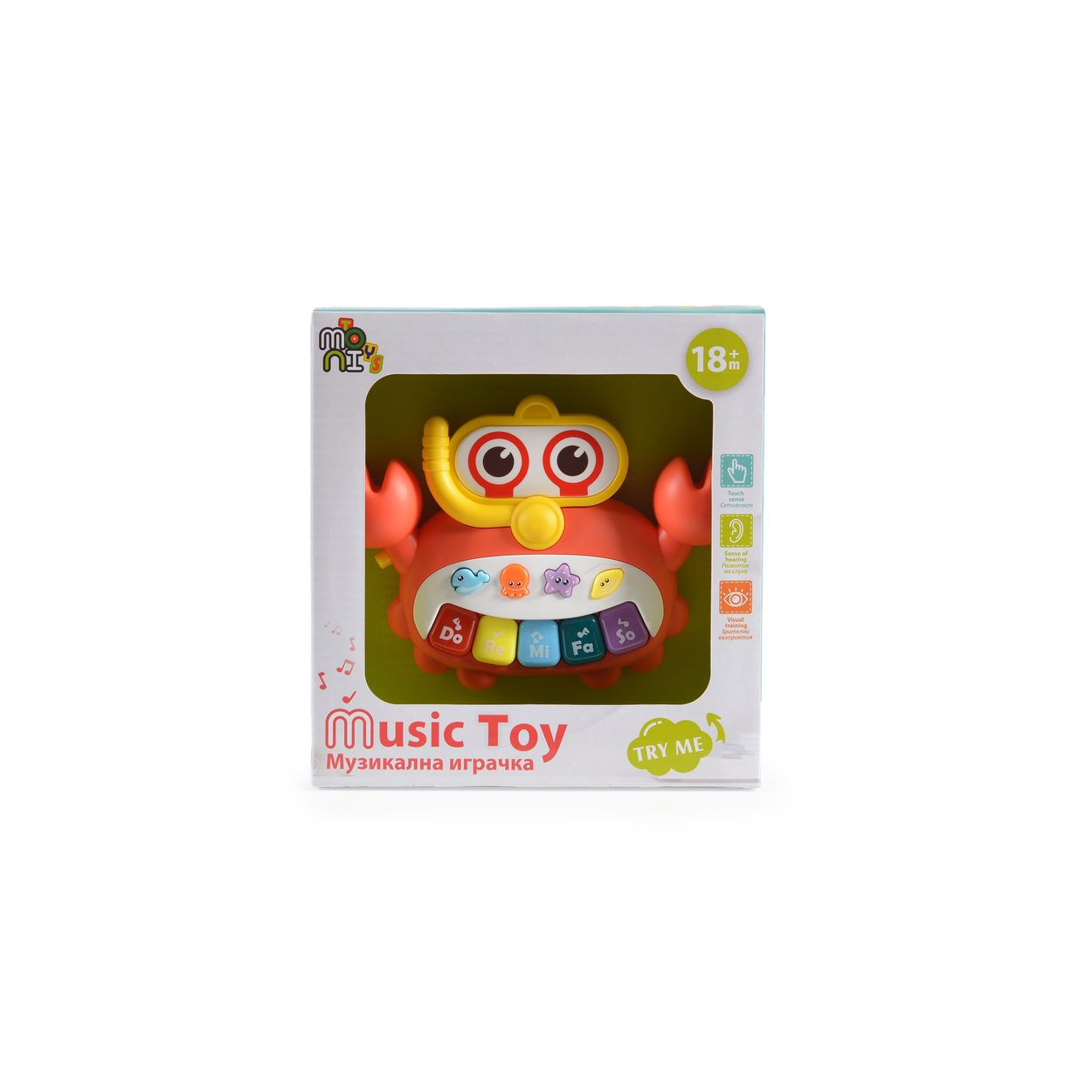 Ein krabbenförmiges Spielzeugklavier in einer Box. Es hat Tasten, Knöpfe und ein Gesicht mit Brille.