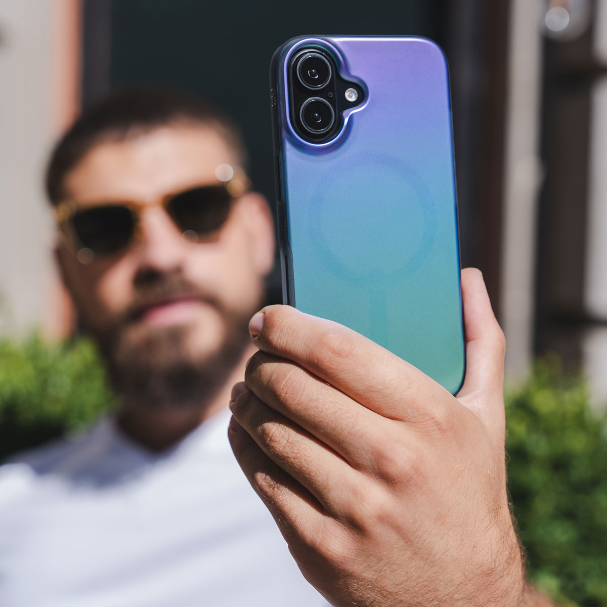 Mann hält Telefon mit Farbverlauf-Hülle. Er trägt eine Sonnenbrille.
