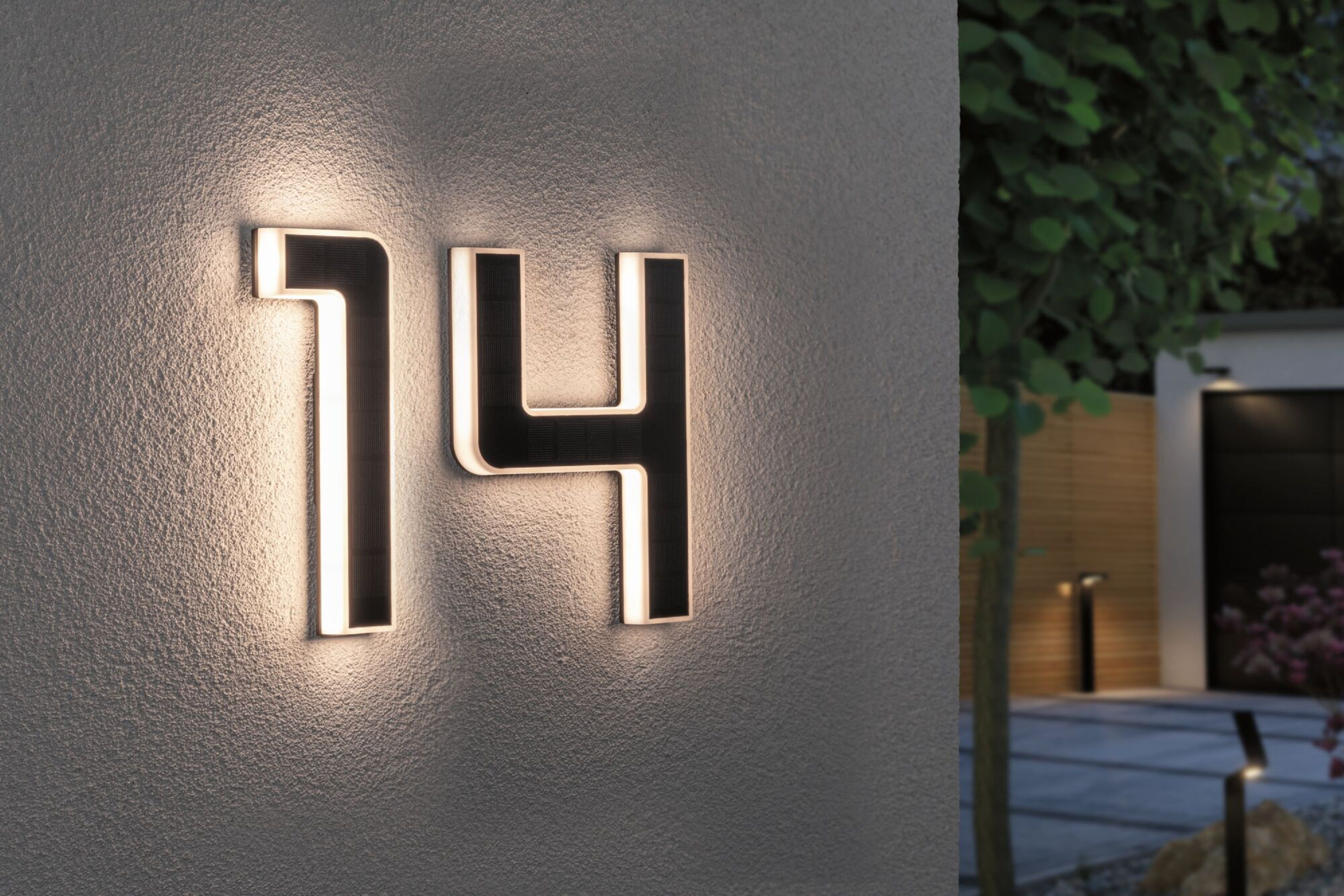 Podświetlony numer domu '14' na ścianie. Jest ciemno, z oświetleniem zewnętrznym i ścieżką.