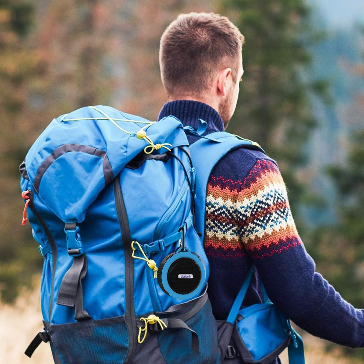 Person trägt Rucksack mit blauem Lautsprecher, in natürlicher Umgebung.