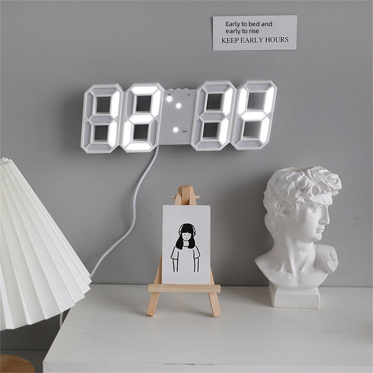 Digitaluhr mit weißen Zahlen, kleine Zeichnung, Büste und Lampe.