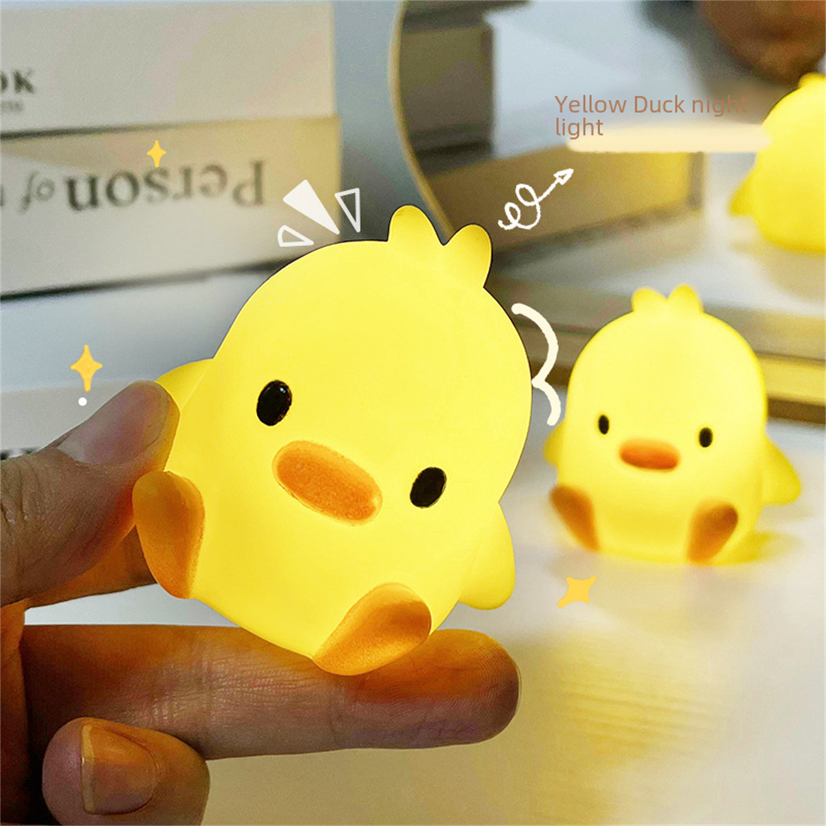 Gelbes Enten-Nachtlicht. Eines wird gehalten, ein anderes im Hintergrund. Beide leuchten und sind süß.