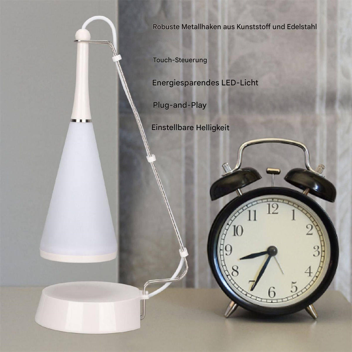 Eine weiße, kegelförmige Lampe schwebt über einem Sockel, in der Nähe eines schwarzen Weckers. Die Lampe hat einen dünnen Tragarm.