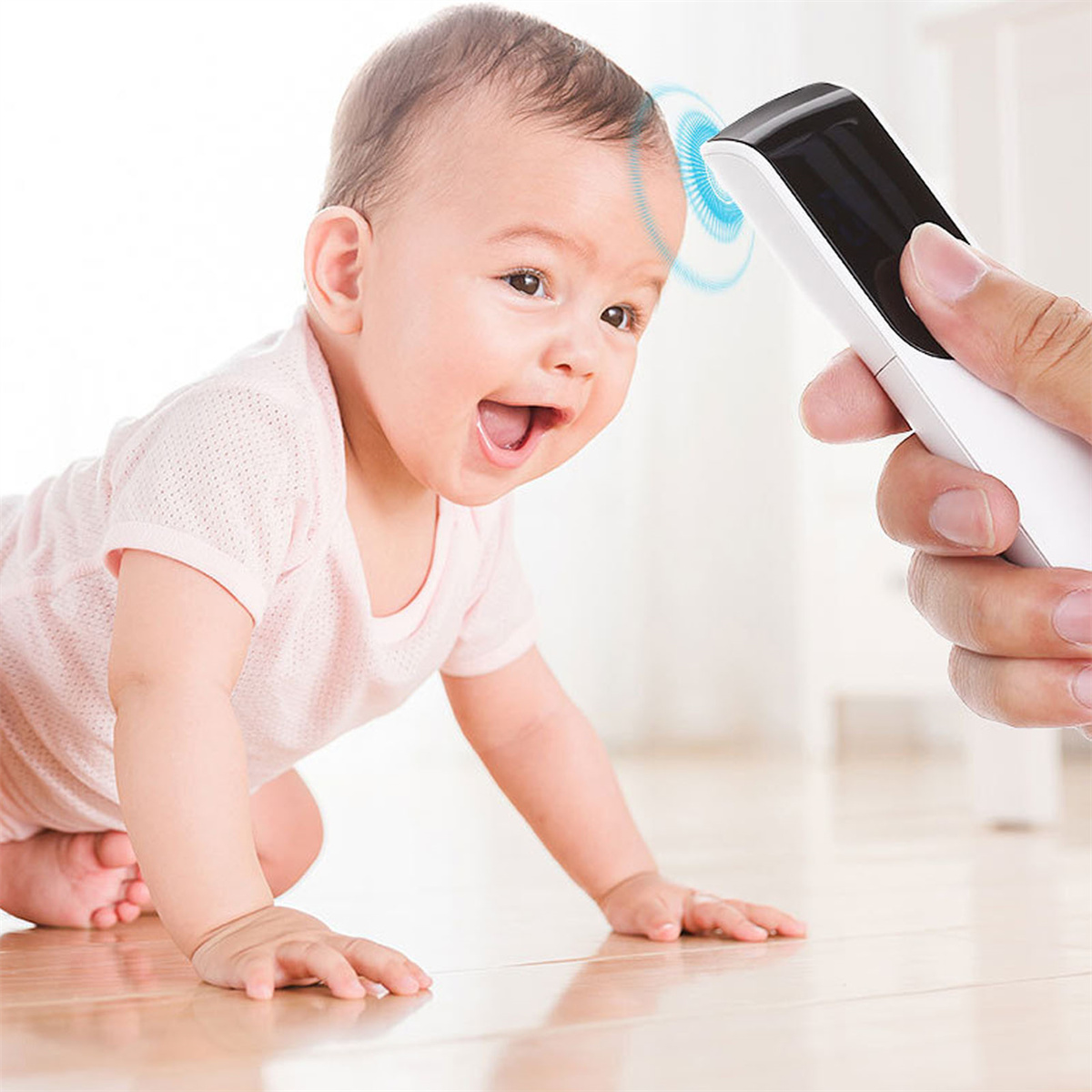 Ein Baby auf dem Boden, das mit einem Thermometer von einer Hand auf Fieber untersucht wird.