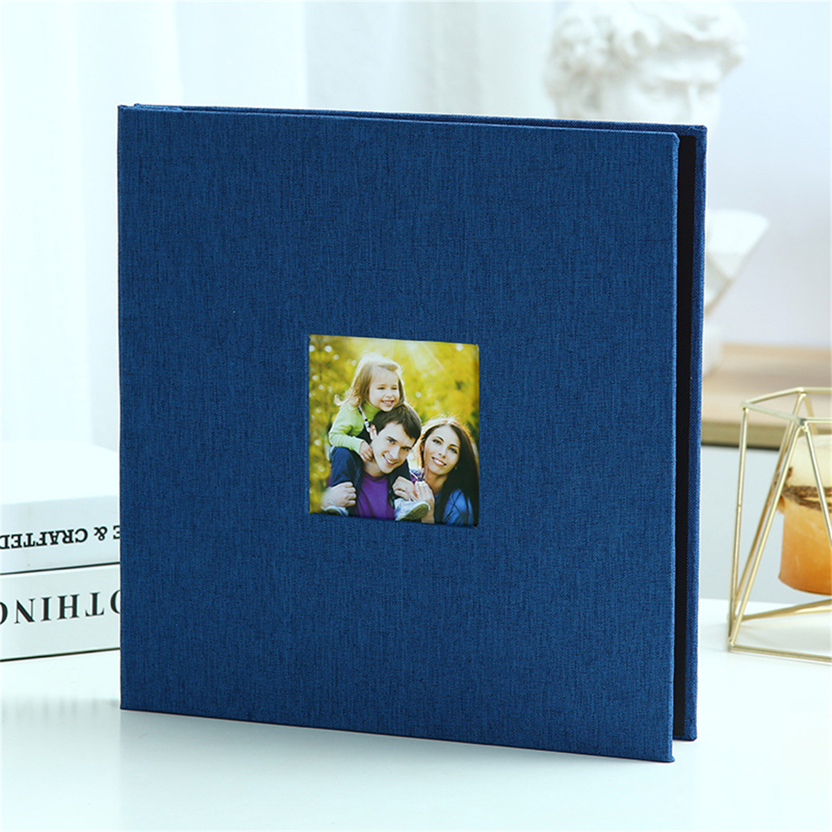 Blaues Fotoalbum mit Familienfoto in quadratischem Rahmen. Bücher und ein goldenes Objekt im Hintergrund.