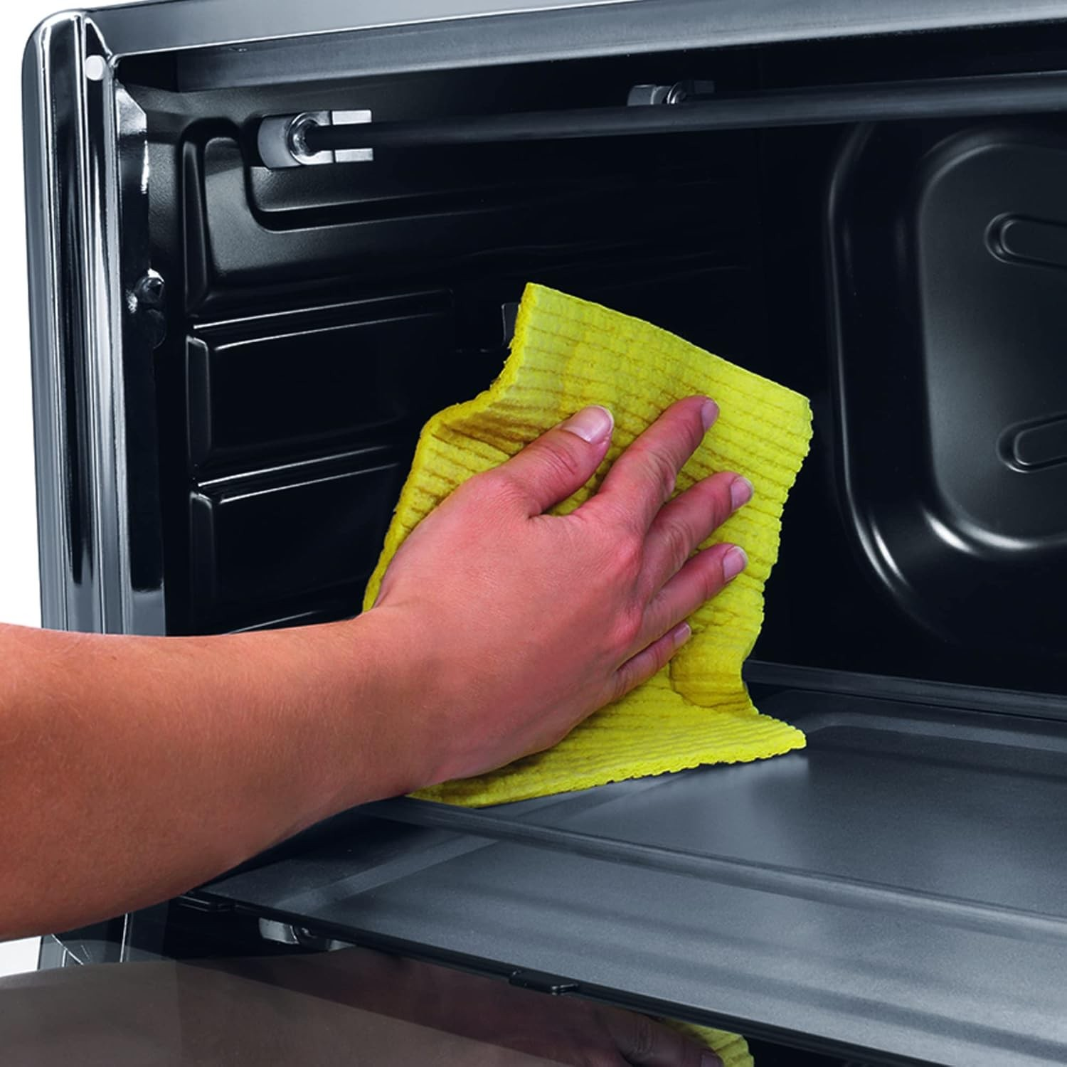 Ręka trzymająca żółtą szmatkę czyszczącą wnętrze czarnego piekarnika.