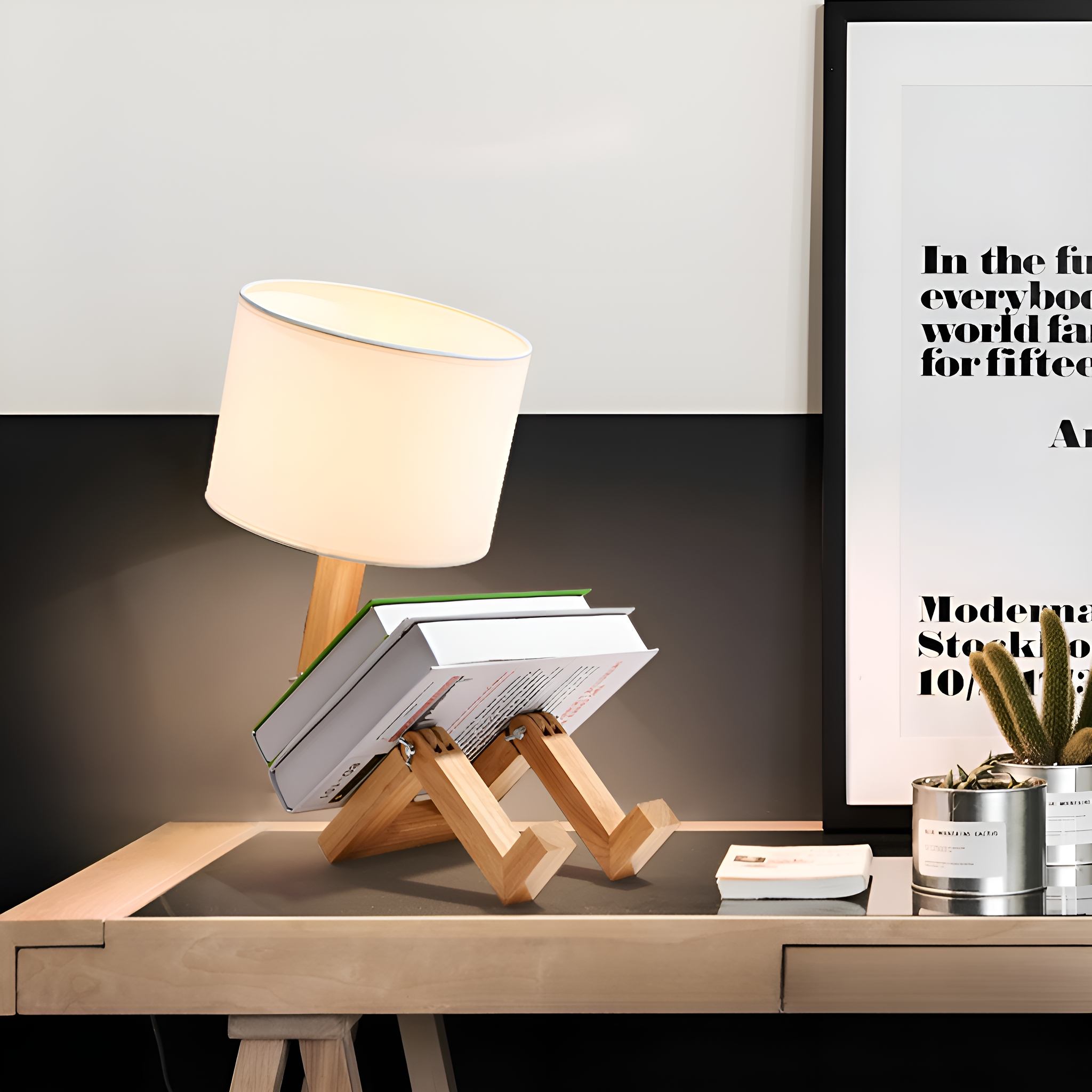 Eine Lampe mit Büchern auf einem Schreibtisch. Im Hintergrund ein Poster und eine kleine Pflanze.