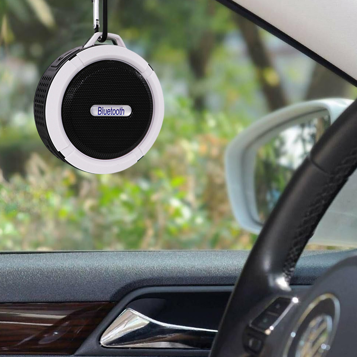 Ein Auto-Innenraum mit einem Bluetooth-Lautsprecher, der an einem Haken hängt; Lenkrad sichtbar.