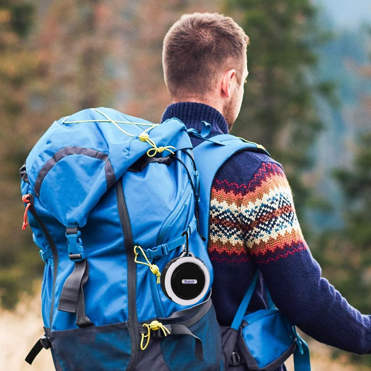 Mann mit Rucksack auf einem Weg, Lautsprecher befestigt. Braune Haare, blauer Rucksack.