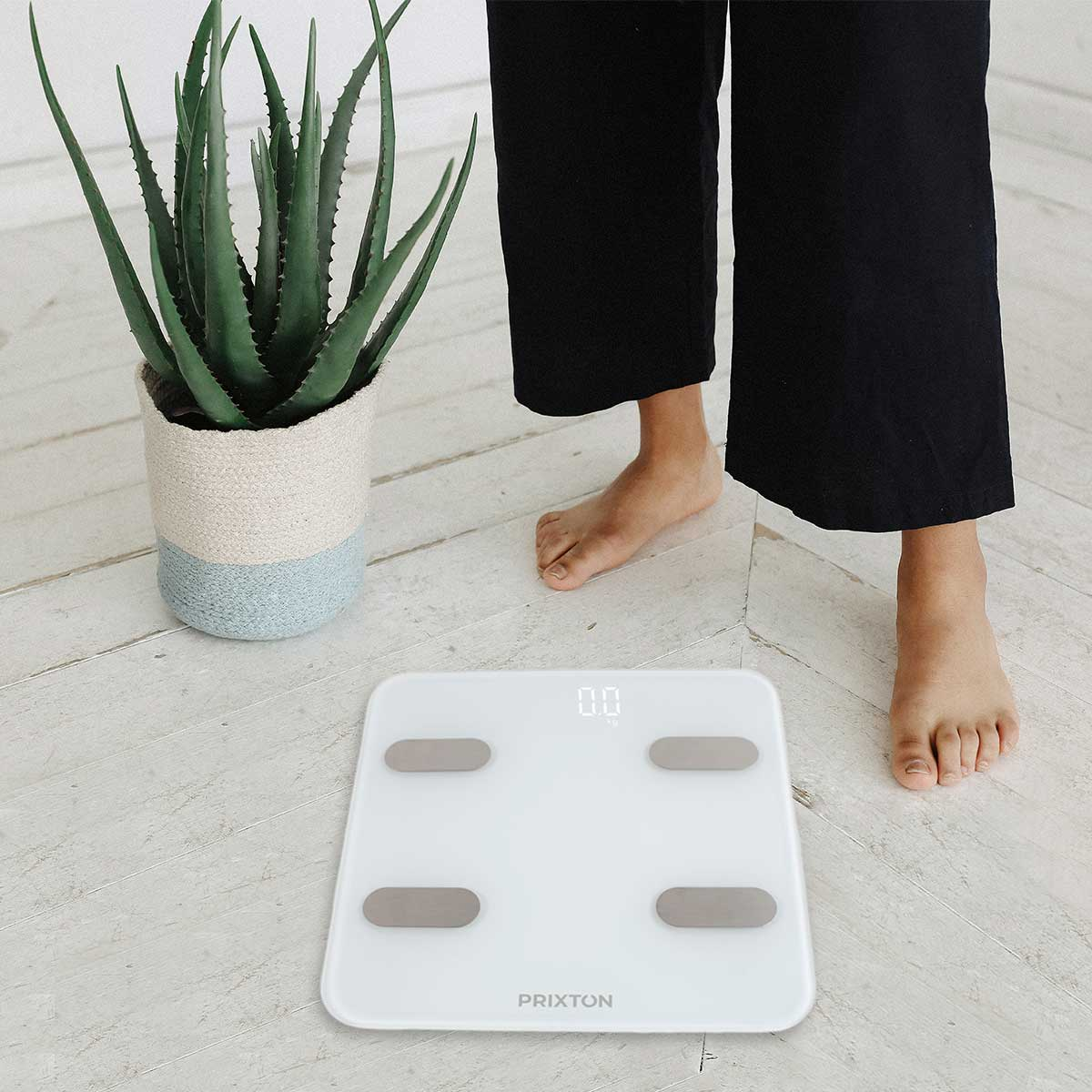 Osoba stojąca na wadze cyfrowej z białą powierzchnią i szarymi przyciskami.