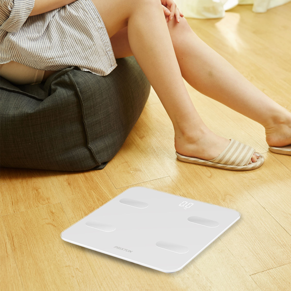 Biała waga na drewnianej podłodze z widocznymi nogami i stopami kobiety. Pokazuje 0,0.