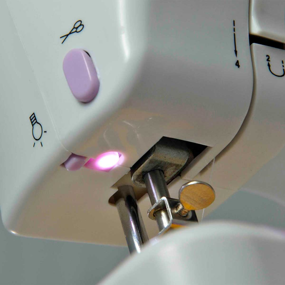 Zbliżenie białej maszyny do szycia z podświetlanym obszarem igły, ikonami nożyczek i żarówki oraz fioletowym przyciskiem.