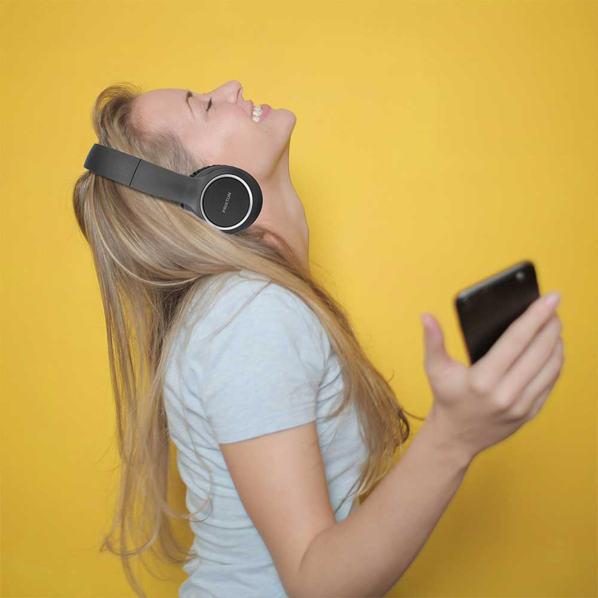 Mujer con auriculares negros escuchando música sobre fondo amarillo.
