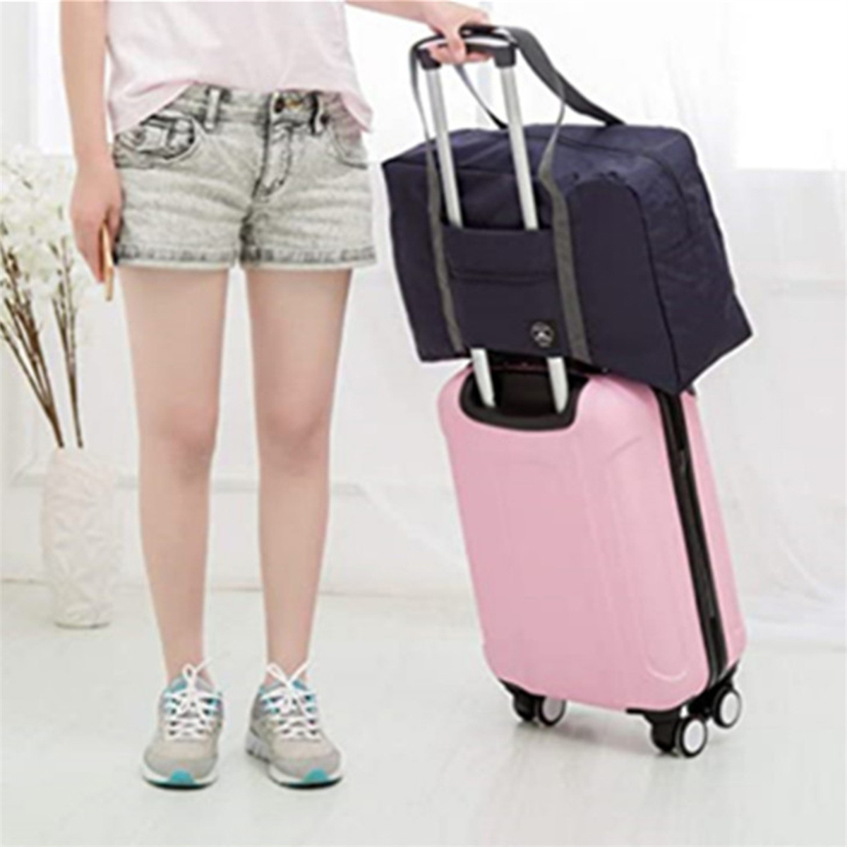 Eine Person hält eine marineblaue Tragetasche auf einem pinkfarbenen Koffer. Die Person trägt Shorts und Turnschuhe.