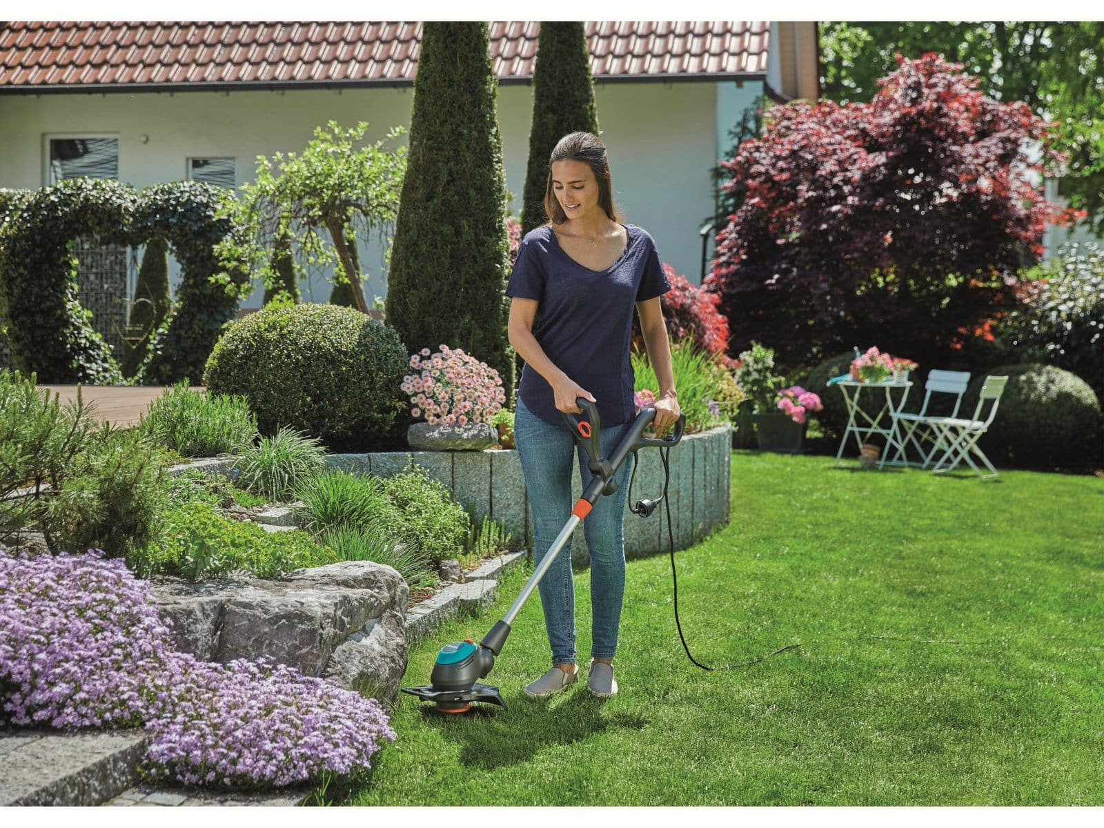 Eine Frau benutzt einen Rasentrimmer in einem Garten mit Pflanzen.