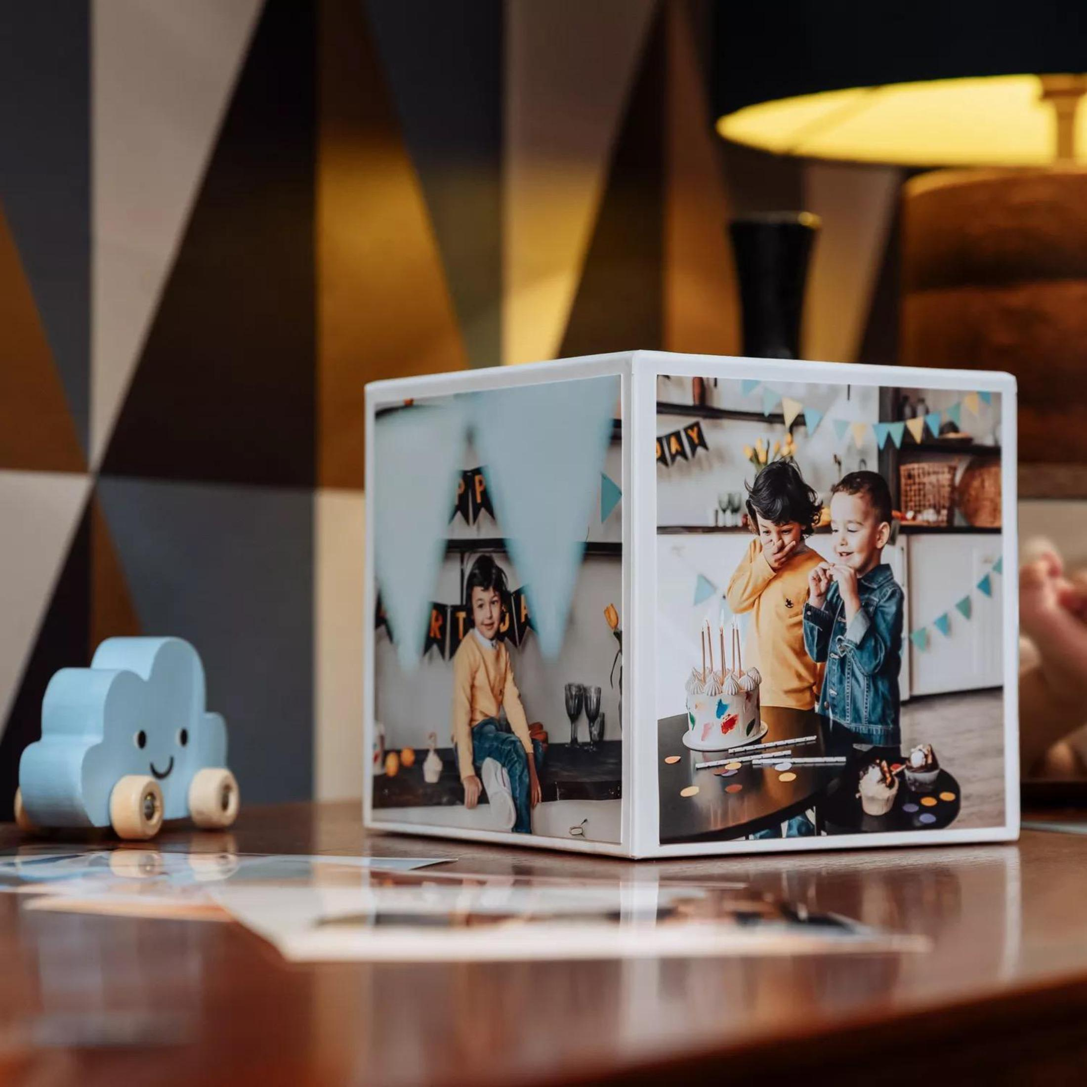 Kostka ze zdjęciami pokazuje zdjęcia dzieci na urodzinach. Niebieska chmura na drewnianym stole.