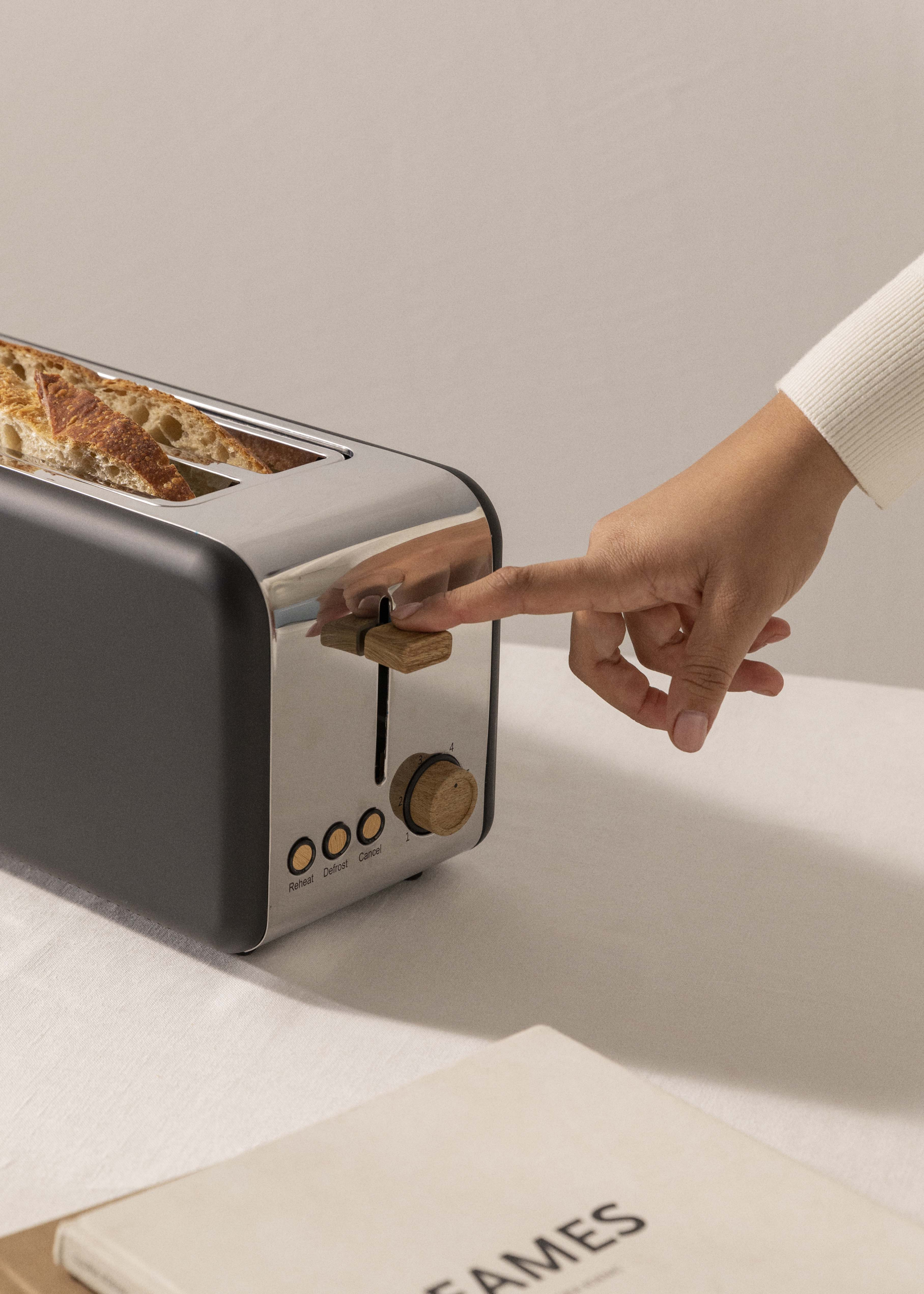 Main d'une personne appuyant sur le levier du grille-pain. Toast à l'intérieur.