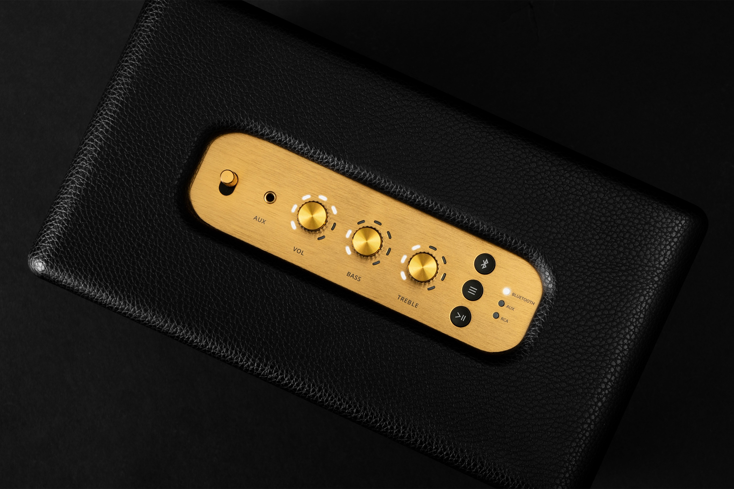 Un altavoz de cuero negro con un panel de control dorado. El panel tiene perillas, botones y un logotipo de la marca.