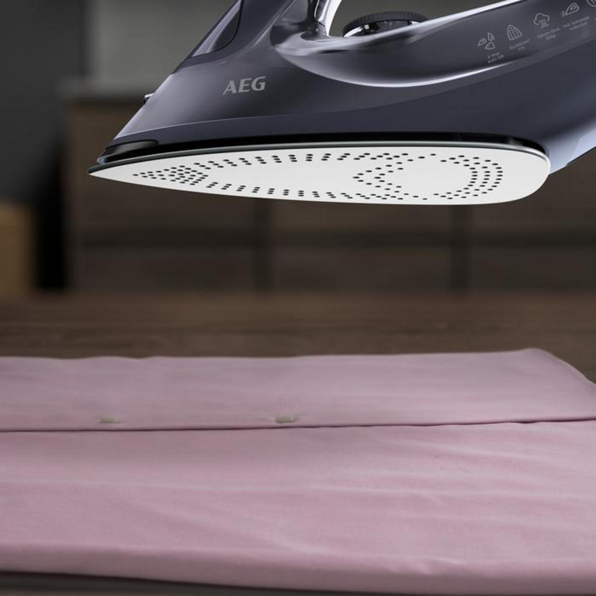 Una plancha flotando sobre una camisa rosa en una superficie de madera. La plancha es negra y blanca.