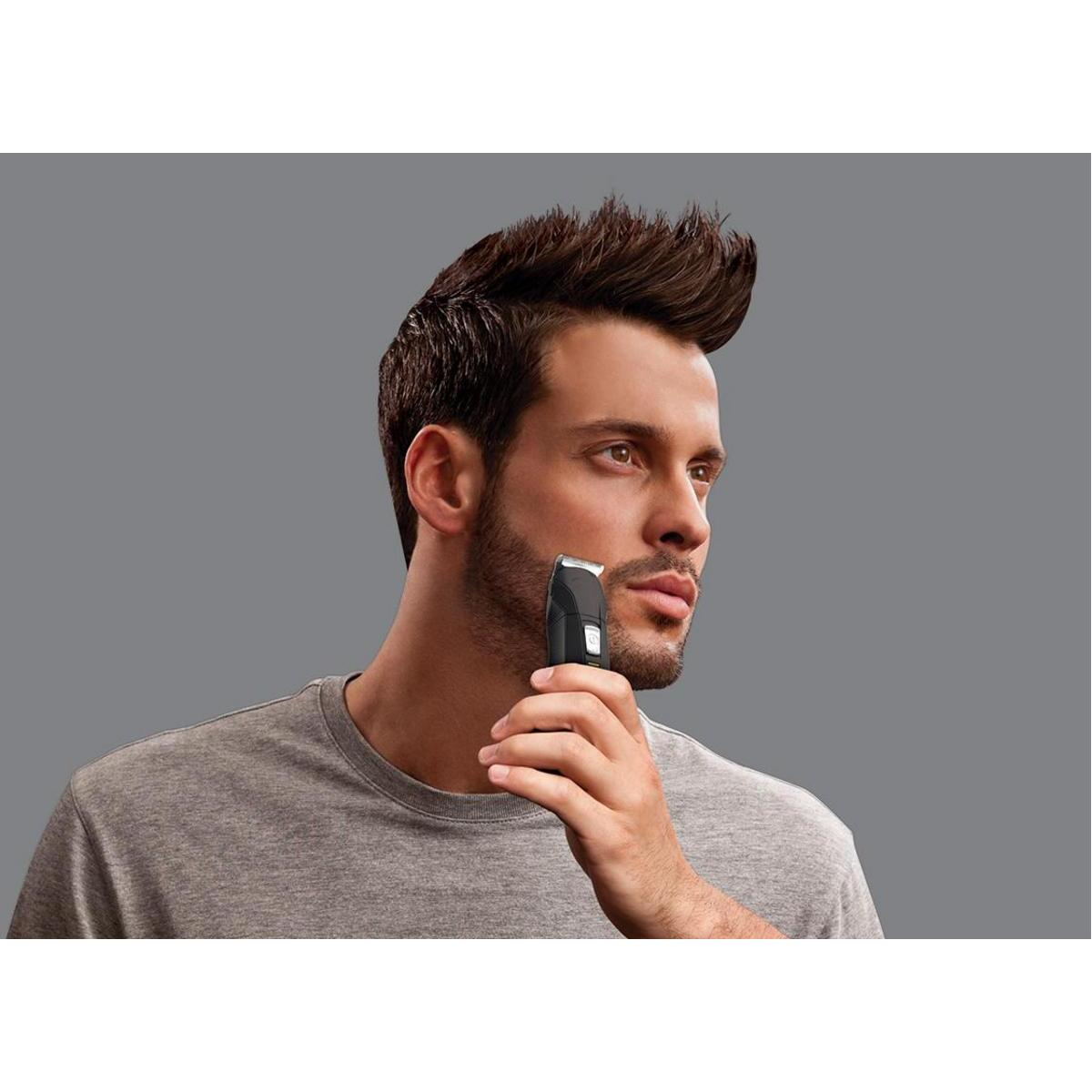 Mężczyzna goli brodę trymerem, na szarym tle.