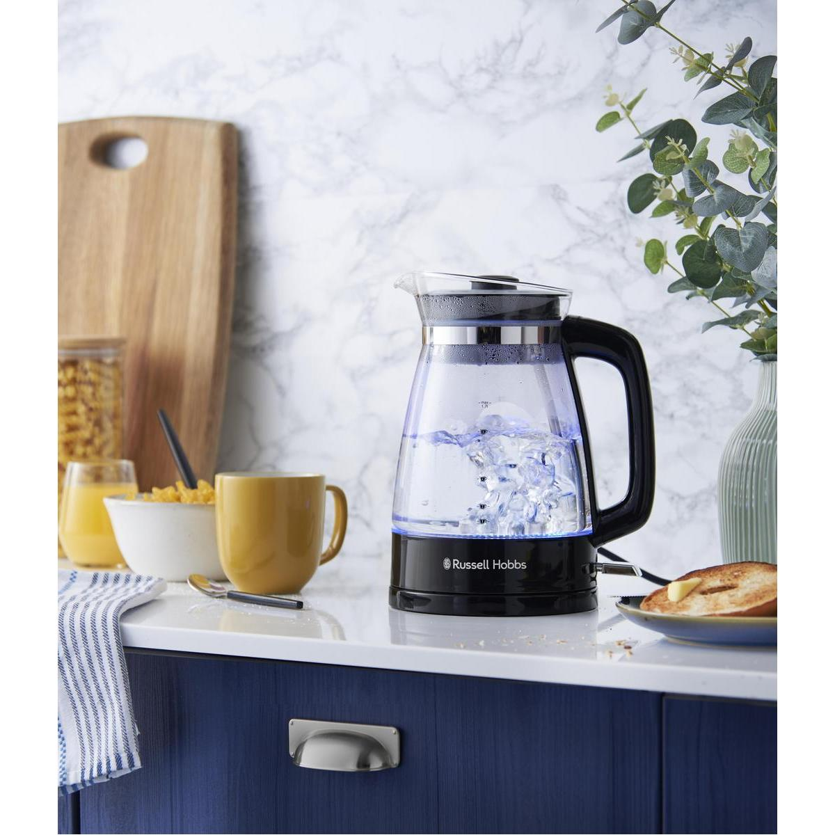 Een glazen elektrische waterkoker met water en blauw licht, met andere keukenartikelen.