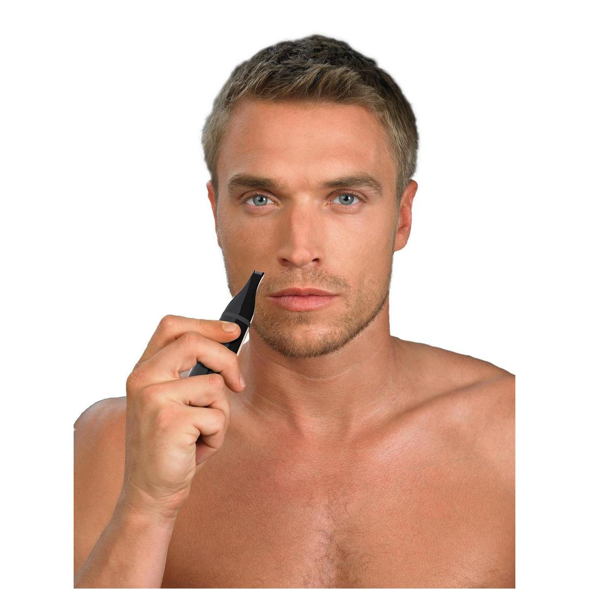 Mann rasiert Bart mit kleinem schwarzen Trimmer. Er ist ohne Hemd, blickt in die Kamera.