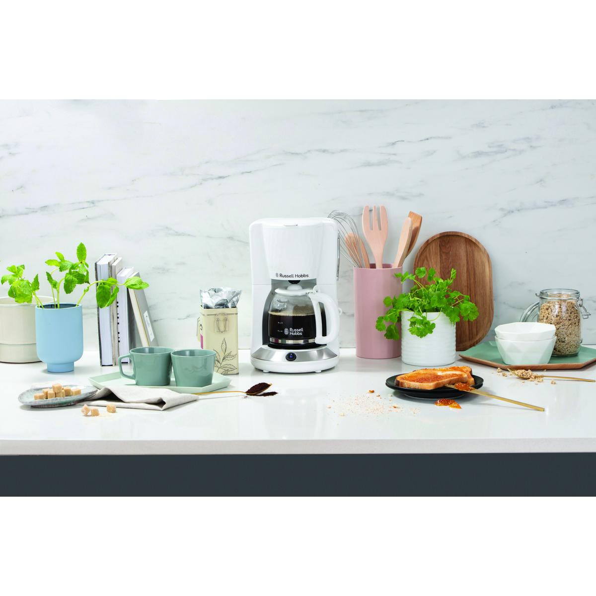 Küchenszene mit weißer Kaffeemaschine, Pflanzen und Frühstückszutaten.