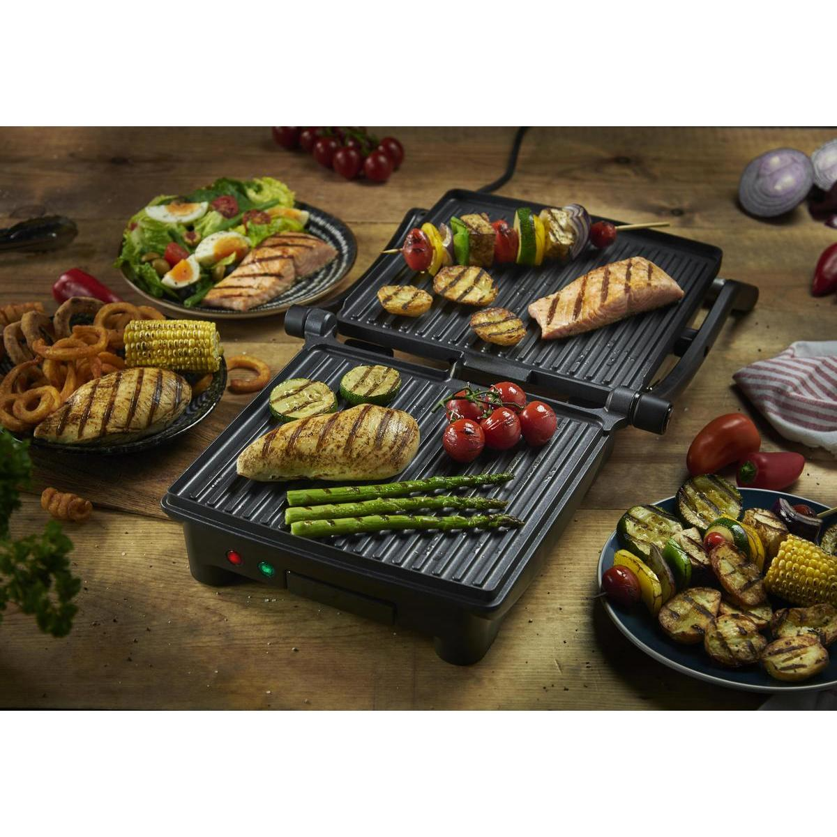 Parrilla con diversos alimentos: pollo, salmón, verduras y brochetas. Platos de comida rodean la parrilla.