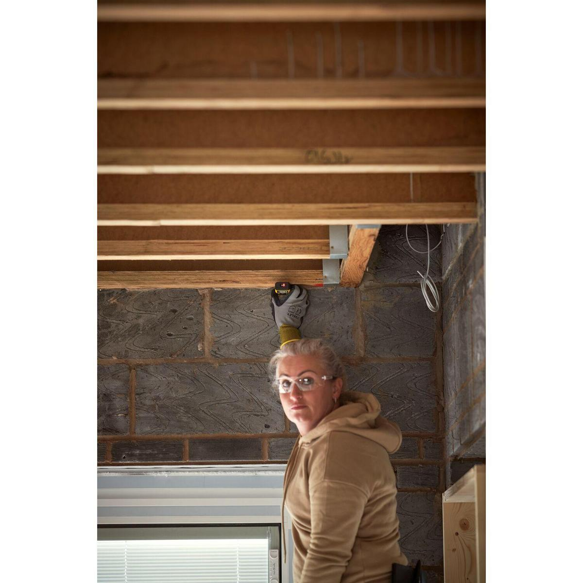 Una mujer con gafas y una sudadera beige mira a la cámara. Está en una habitación con vigas de madera y ladrillos.