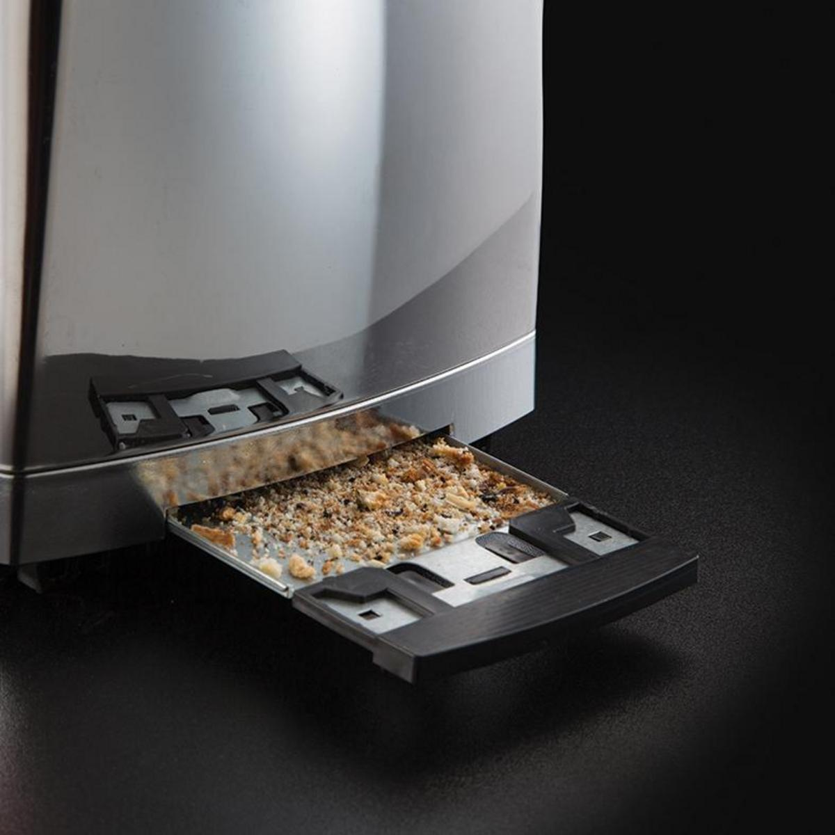 Toster ze stali nierdzewnej z tacką na okruchy. Tacka jest wysunięta, widać okruchy chleba. Czarne tło.