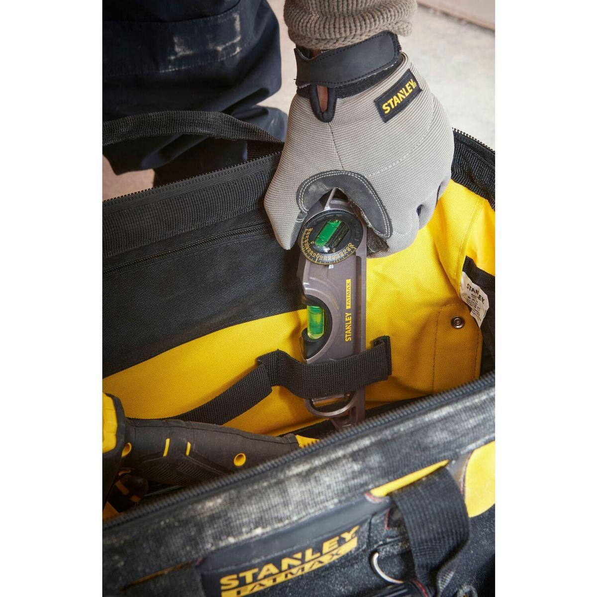 Hand mit Handschuh hält eine Wasserwaage in einer Werkzeugtasche. Gelber Innenraum, schwarze Tasche.