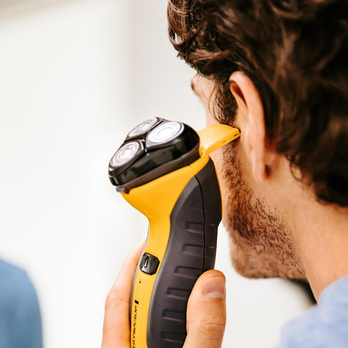 Un uomo si rade la barba con un rasoio elettrico giallo e nero.